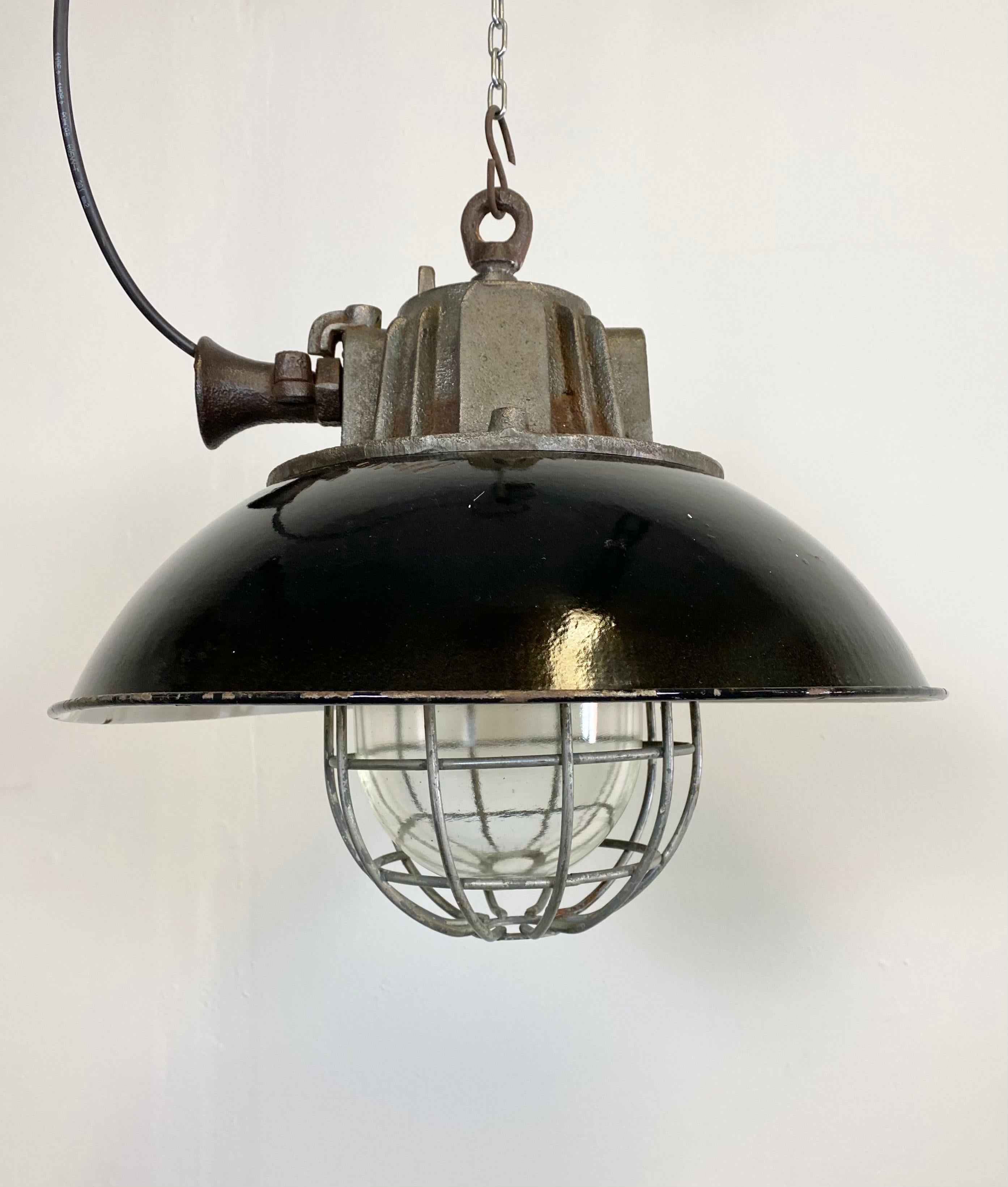 Industrial hanging lamp manufactured during the 1950s in former Czechoslovakia. It features a black enamel shade, white enamel interior, cast iron top, clear glass cover and iron grid. Porcelain socket for E 27 lightbulbs and new wire. The weight of