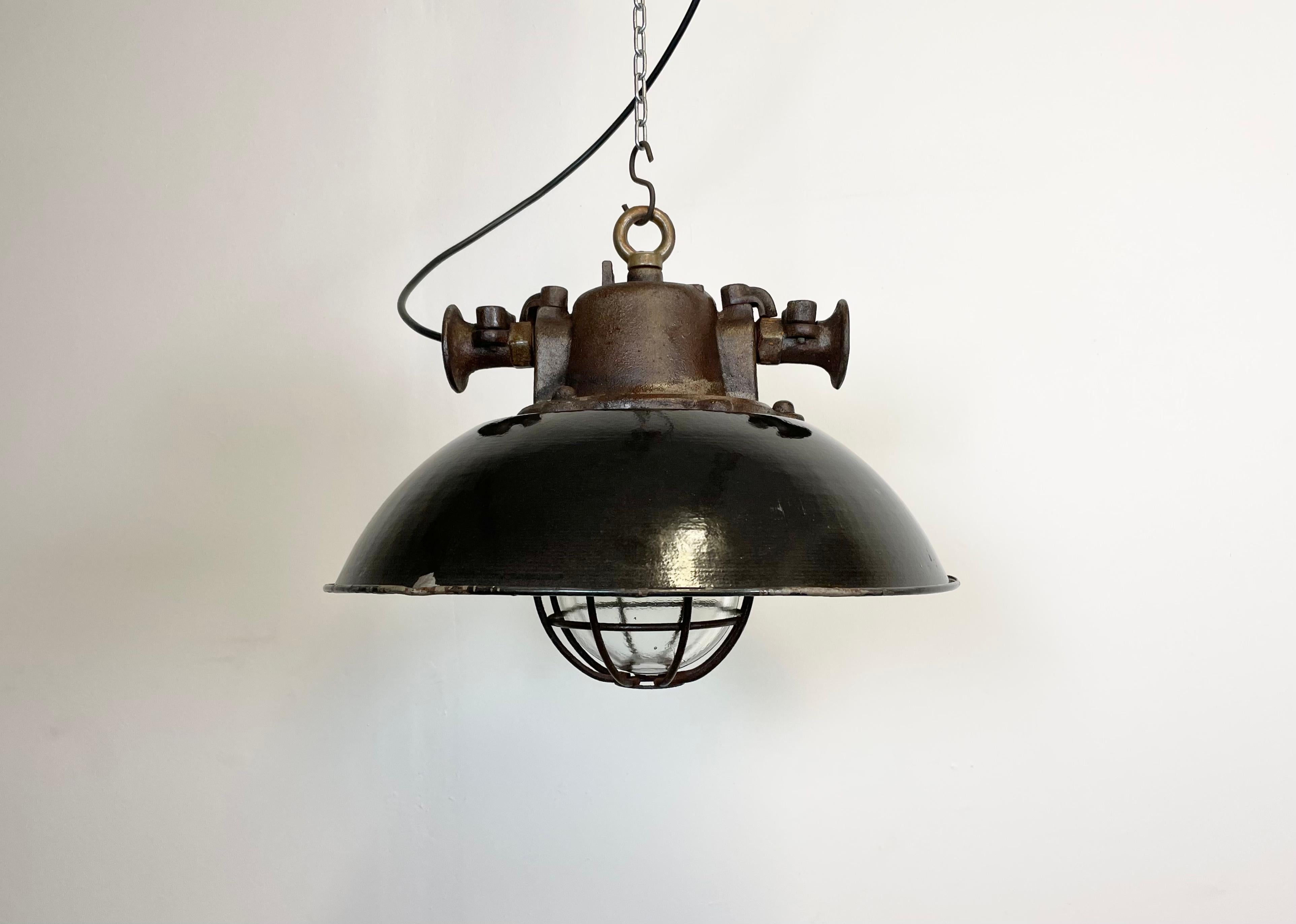 Industrial rusty hanging lamp manufactured during the 1950s in former Czechoslovakia. It features a black enamel shade, white enamel interior, cast iron top, clear glass cover and iron grid. Porcelain socket for E 27 lightbulbs and new wire. The