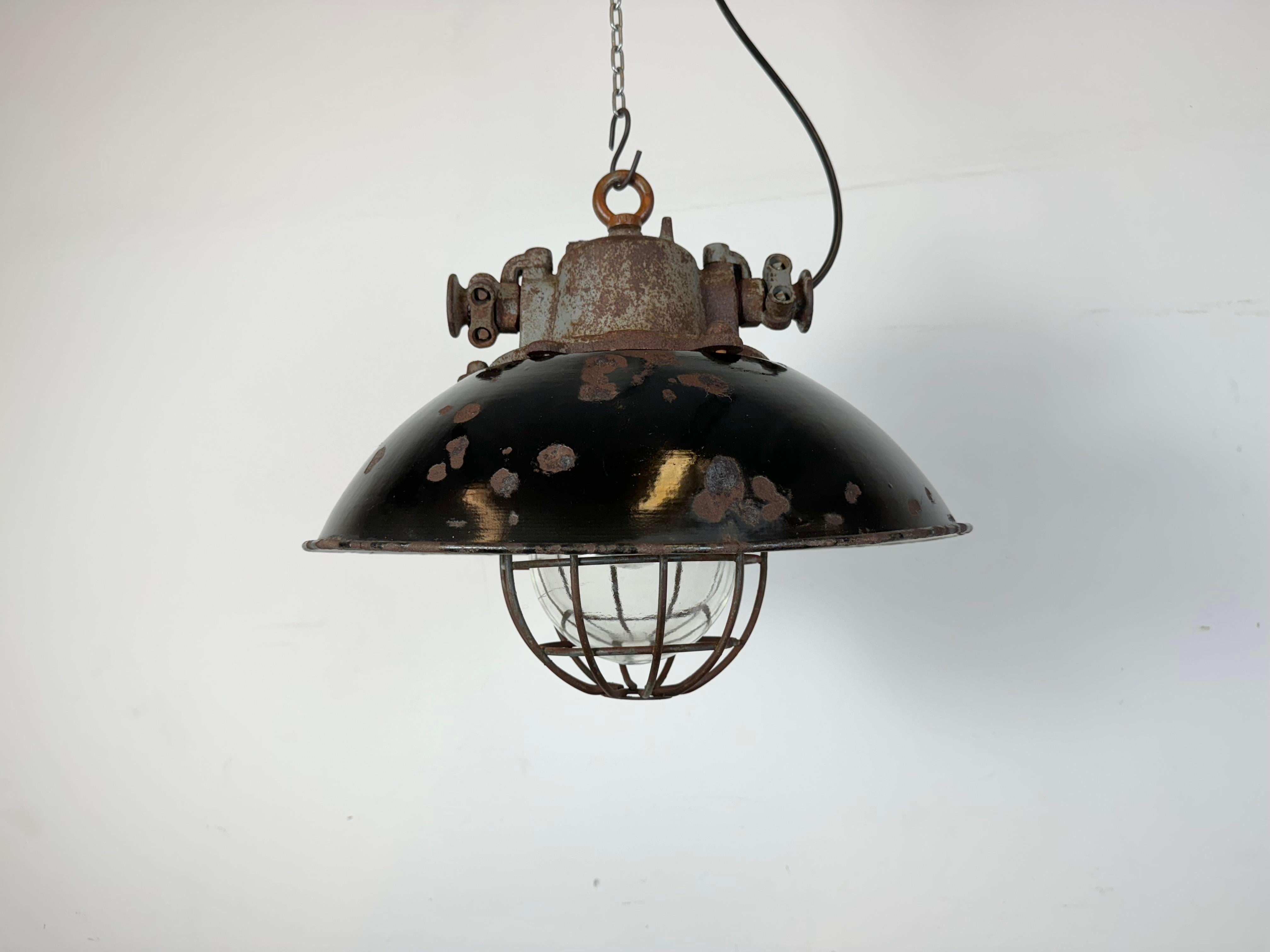 Industrial hanging lamp manufactured by Elektrosvit in former Czechoslovakia during the 1960s. It features a black enamel shade, with white enamel interior, a cast iron top, a clear glass cover and an iron grid.The porcelain socket requires standard