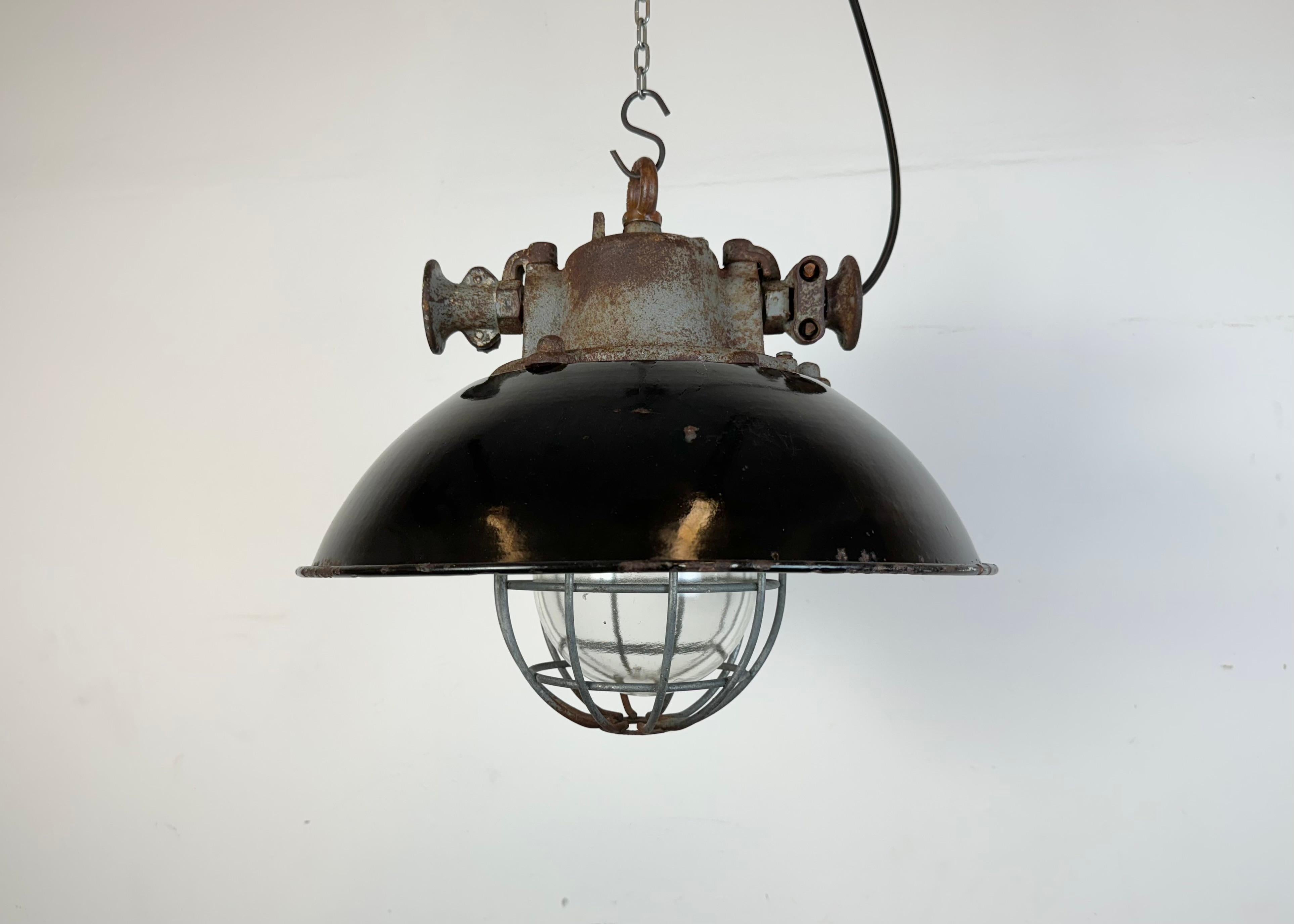 Industrial hanging lamp manufactured by Elektrosvit in former Czechoslovakia during the 1960s. It features a black enamel shade, with white enamel interior, a cast iron top, a clear glass cover and an iron grid.The porcelain socket requires standard