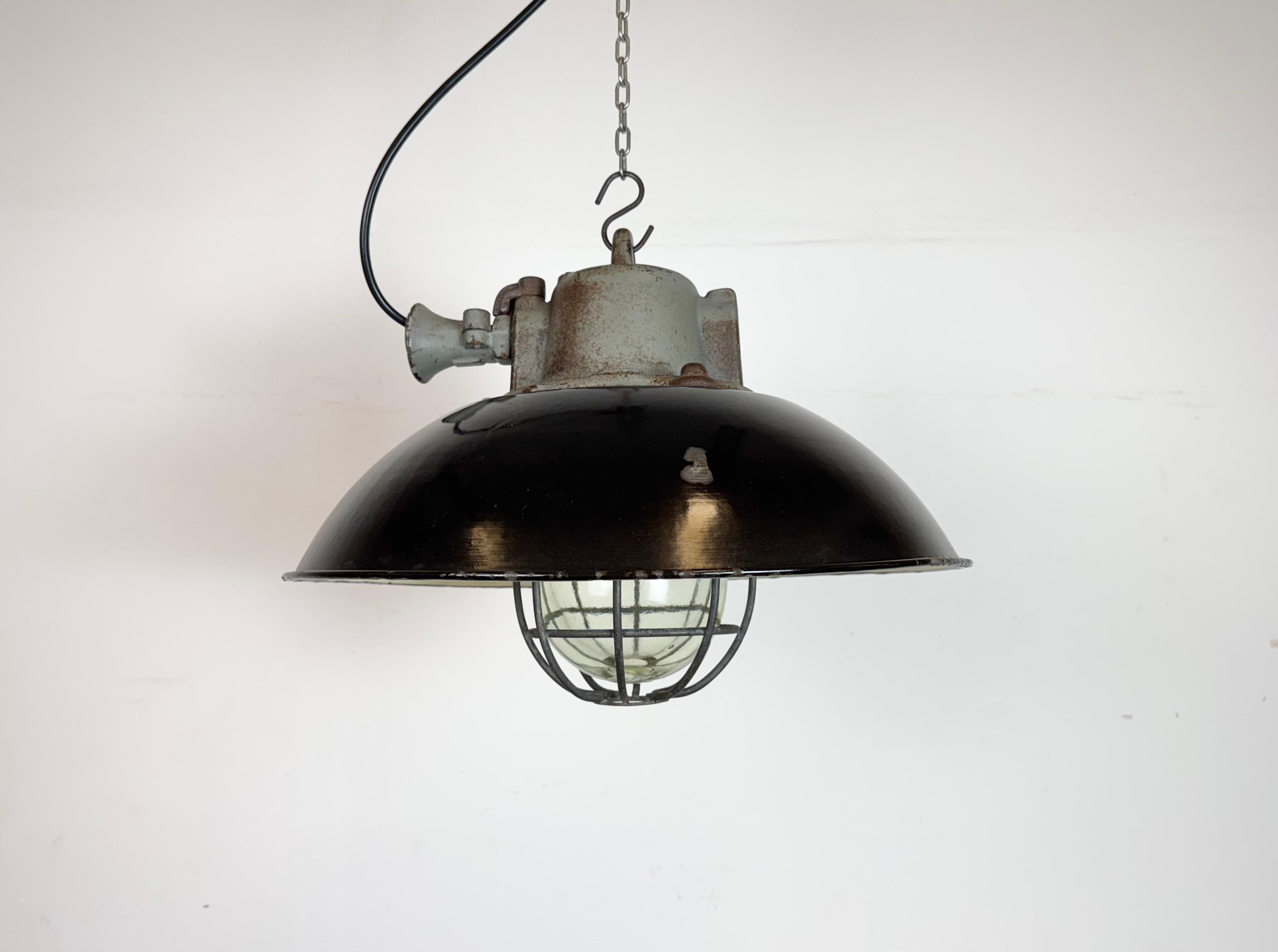 Lámpara industrial colgante fabricada por Elektrosvit en la antigua Checoslovaquia durante la década de 1960. Tiene una pantalla de esmalte negro, con el interior de esmalte blanco, la parte superior de hierro fundido, una tapa de cristal
