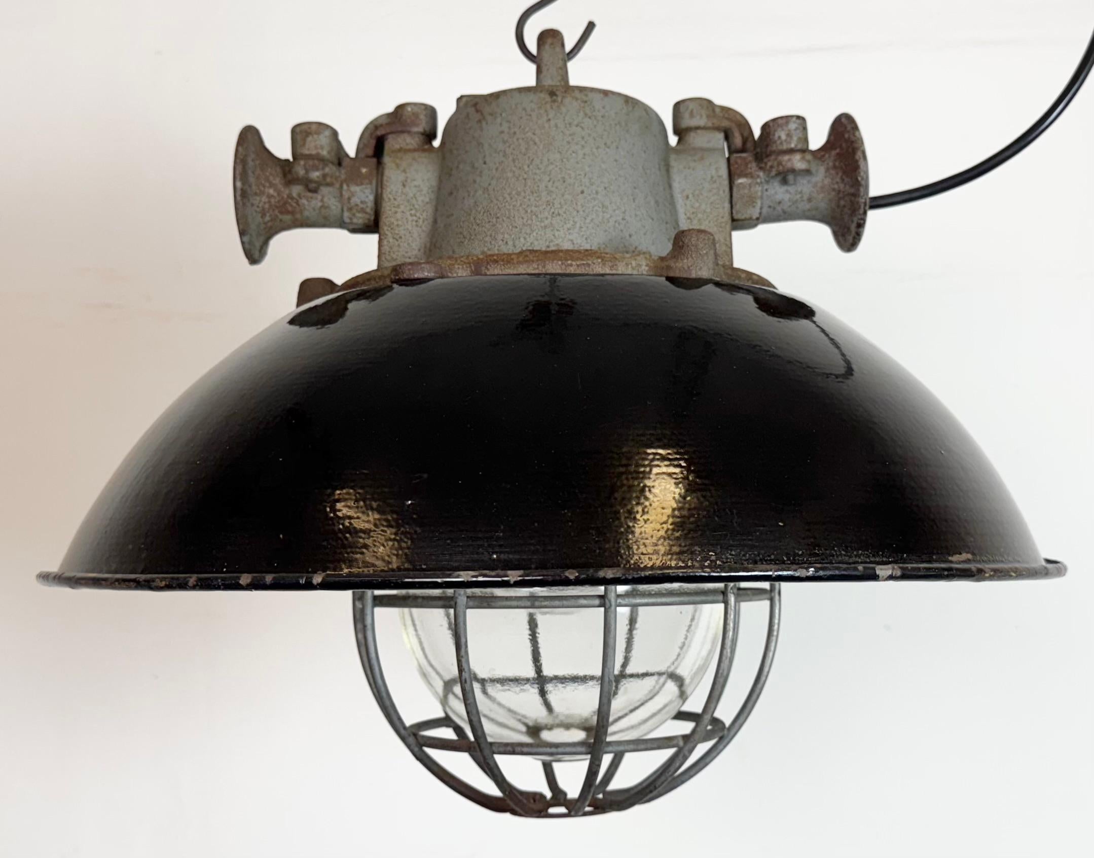Lámpara industrial colgante fabricada por Elektrosvit en la antigua Checoslovaquia durante la década de 1960. Tiene una pantalla de esmalte negro, con el interior de esmalte blanco, la parte superior de hierro fundido, una tapa de cristal