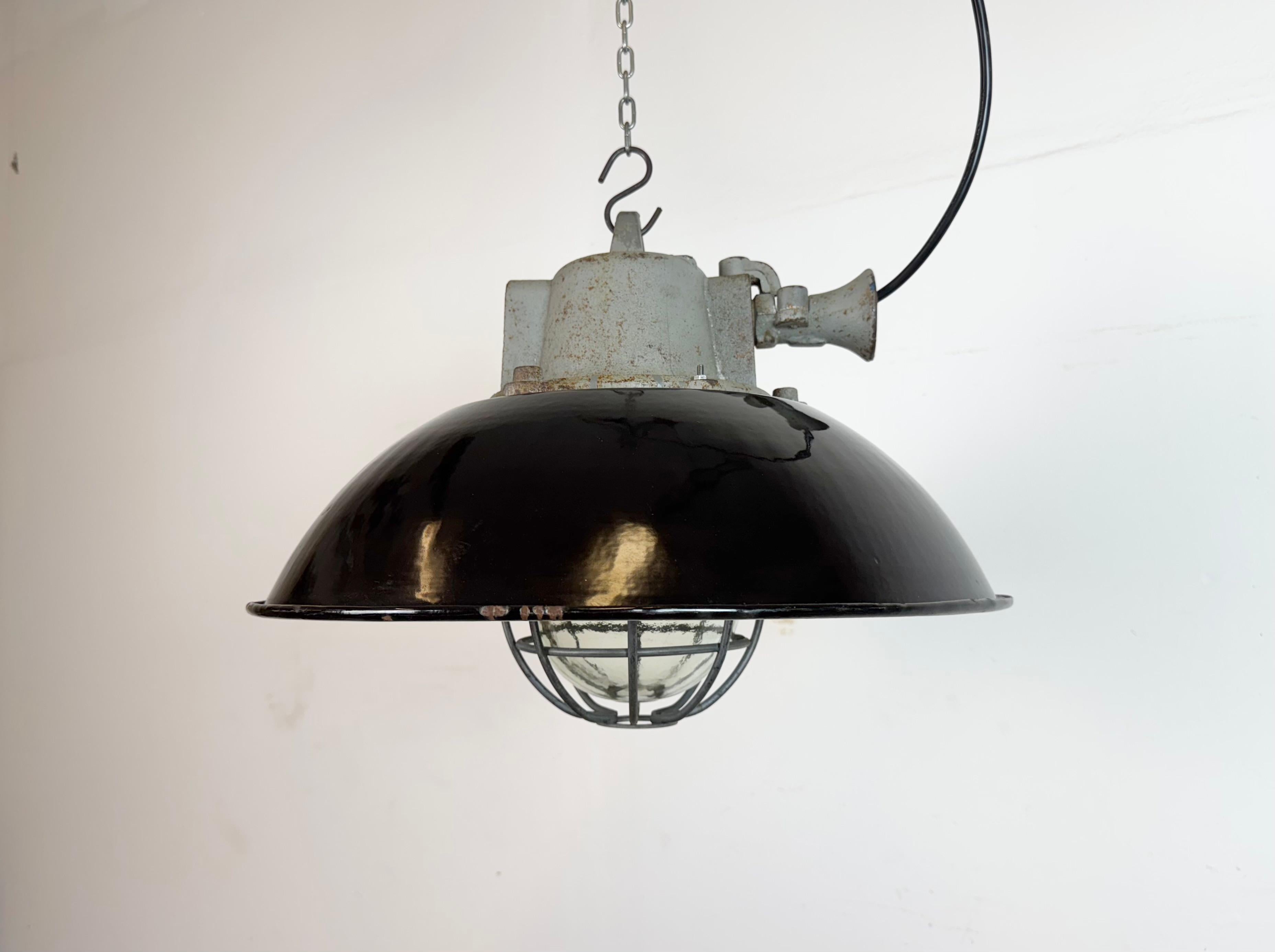 Lampada a sospensione industriale prodotta da Elektrosvit nell'ex Cecoslovacchia negli anni Sessanta. Presenta un paralume in smalto nero, un interno in smalto bianco, un piano in ghisa, un coperchio in vetro trasparente e una griglia in