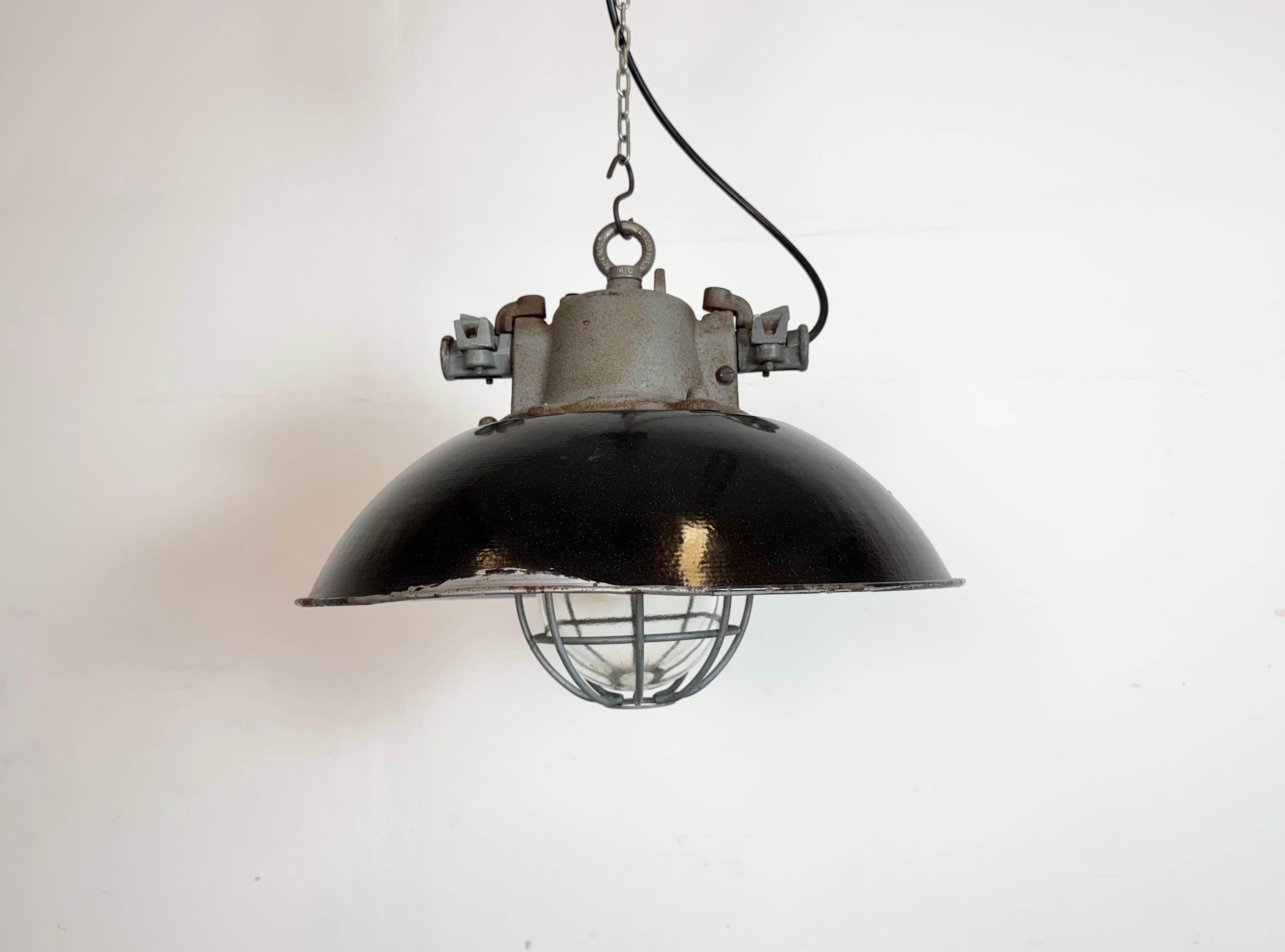 Lámpara industrial colgante fabricada por Elektrosvit en la antigua Checoslovaquia durante la década de 1960. Tiene una pantalla de esmalte negro, con el interior de esmalte blanco, la parte superior de hierro fundido, una tapa de cristal