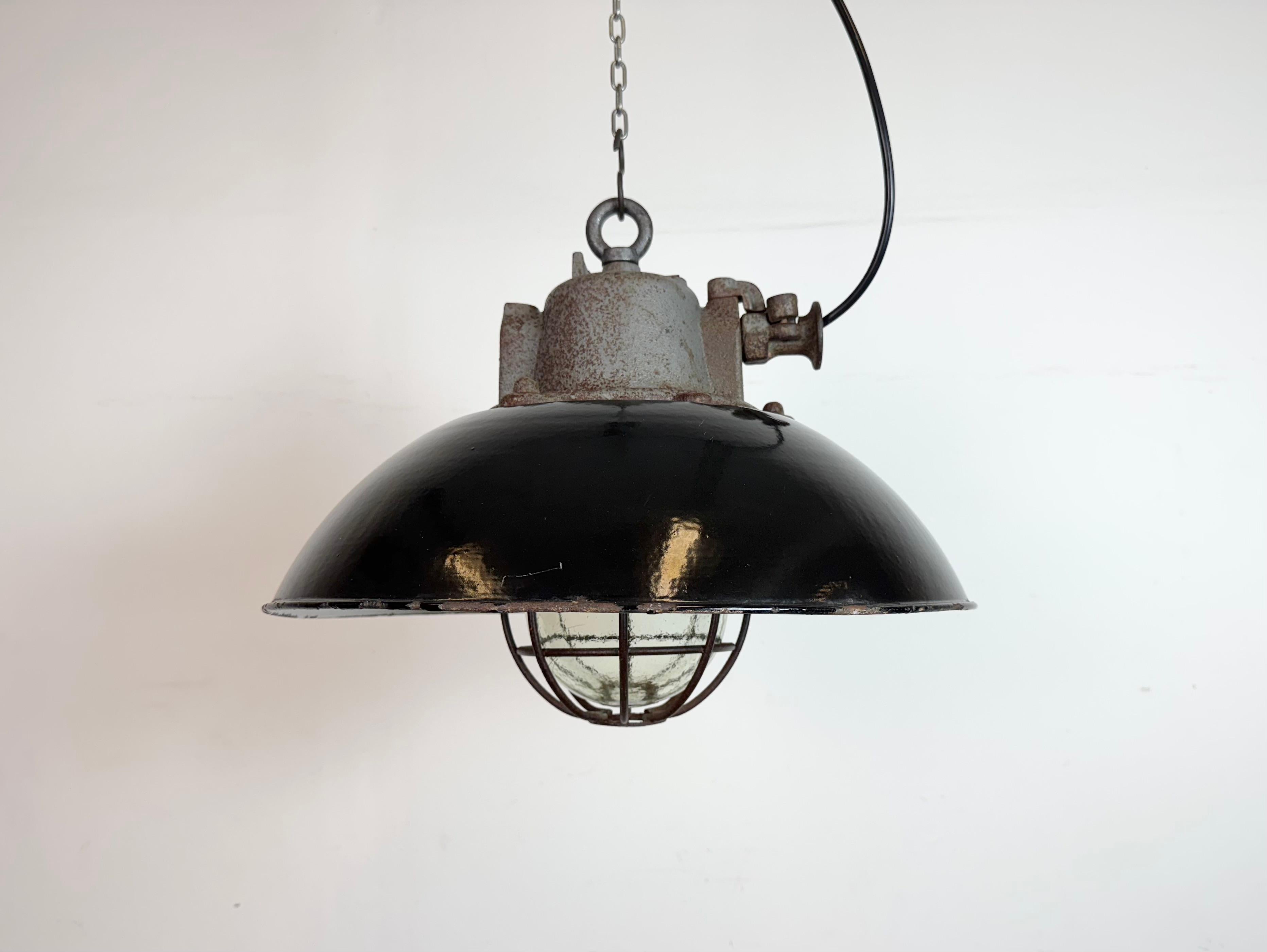 Lampada a sospensione industriale prodotta da Elektrosvit nell'ex Cecoslovacchia negli anni Sessanta. Presenta un paralume in smalto nero, un interno in smalto bianco, un piano in ghisa, un coperchio in vetro trasparente e una griglia in