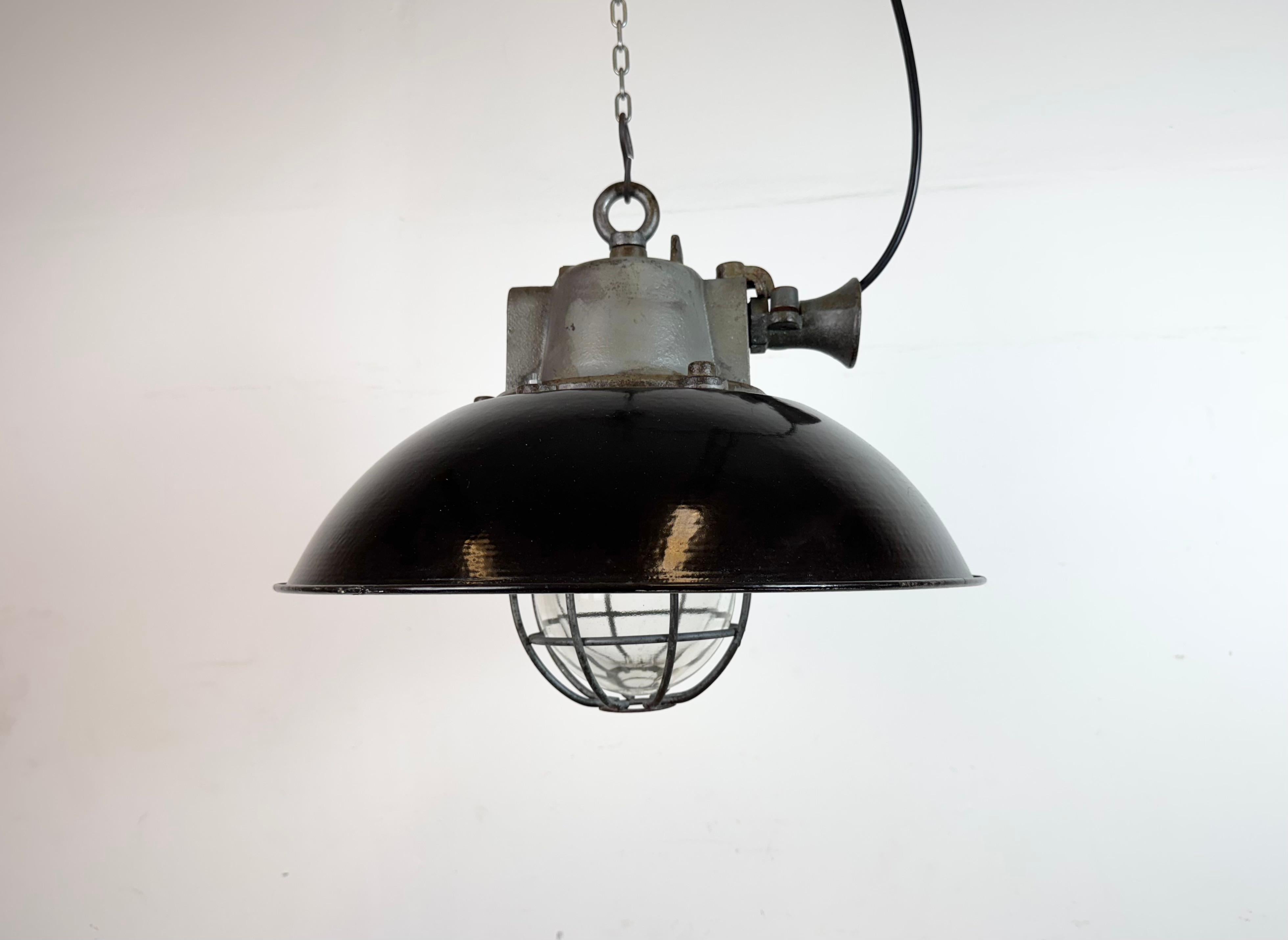 Lampada a sospensione industriale prodotta da Elektrosvit nell'ex Cecoslovacchia negli anni Sessanta. Presenta un paralume in smalto nero, un interno in smalto bianco, un piano in ghisa, un coperchio in vetro trasparente e una griglia in