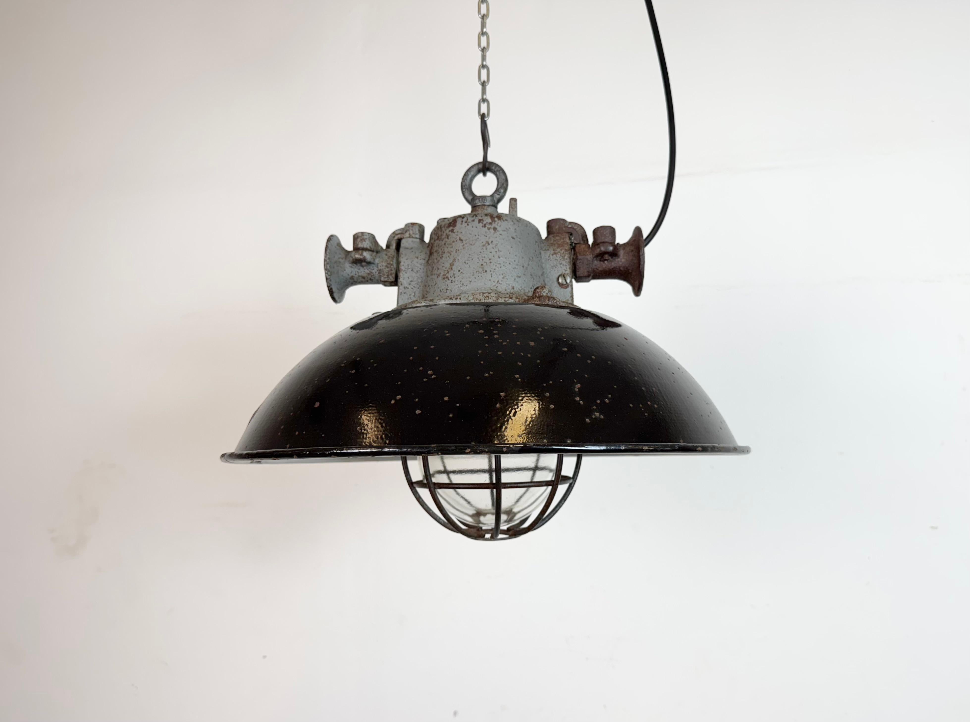 Lámpara industrial colgante fabricada por Elektrosvit en la antigua Checoslovaquia durante la década de 1960. Tiene una pantalla de esmalte negro, con el interior de esmalte blanco, la parte superior de hierro fundido, una tapa de cristal