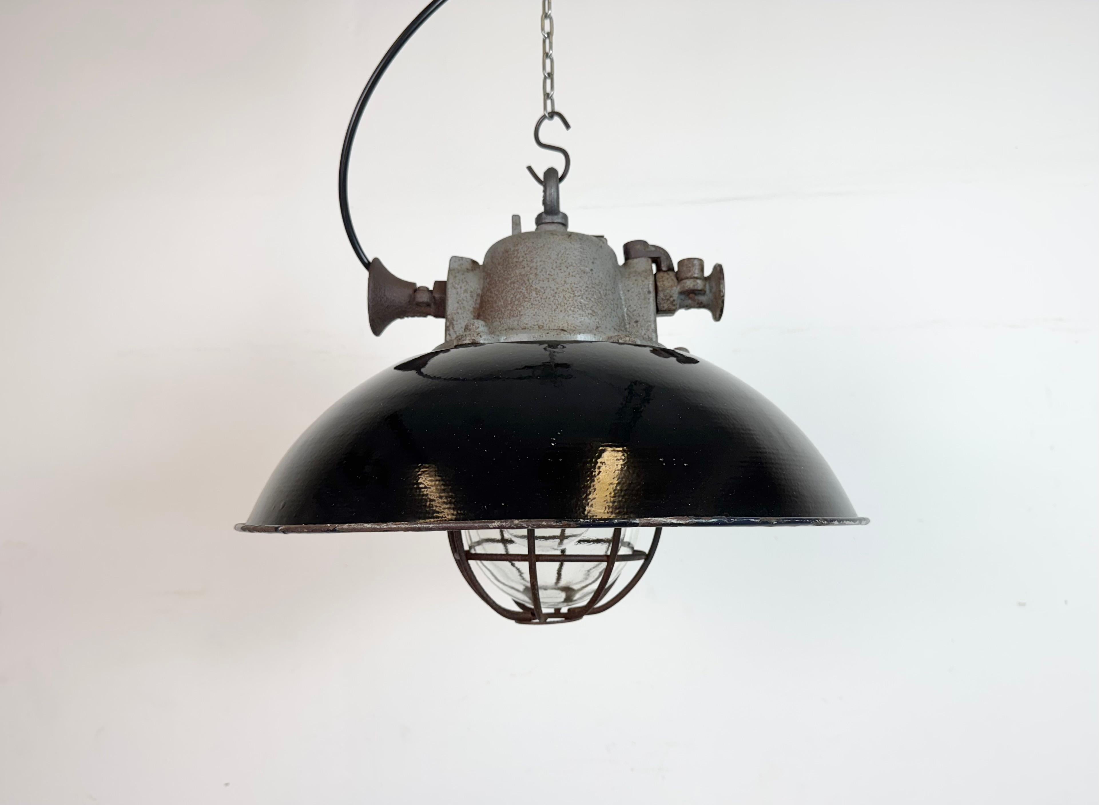 Lámpara industrial colgante fabricada por Elektrosvit en la antigua Checoslovaquia durante la década de 1960. Tiene una pantalla de esmalte negro, con el interior de esmalte blanco, la parte superior de hierro fundido, una tapa de cristal