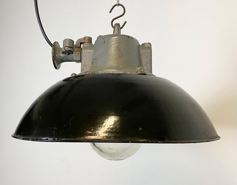 Industrial hanging lamp manufactured during the 1960s in former Czechoslovakia. It features a black enamel shade, white enamel interior, cast iron top and clear glass cover Porcelain socket for E 27 lightbulbs and new wire. The weight of the lamp is