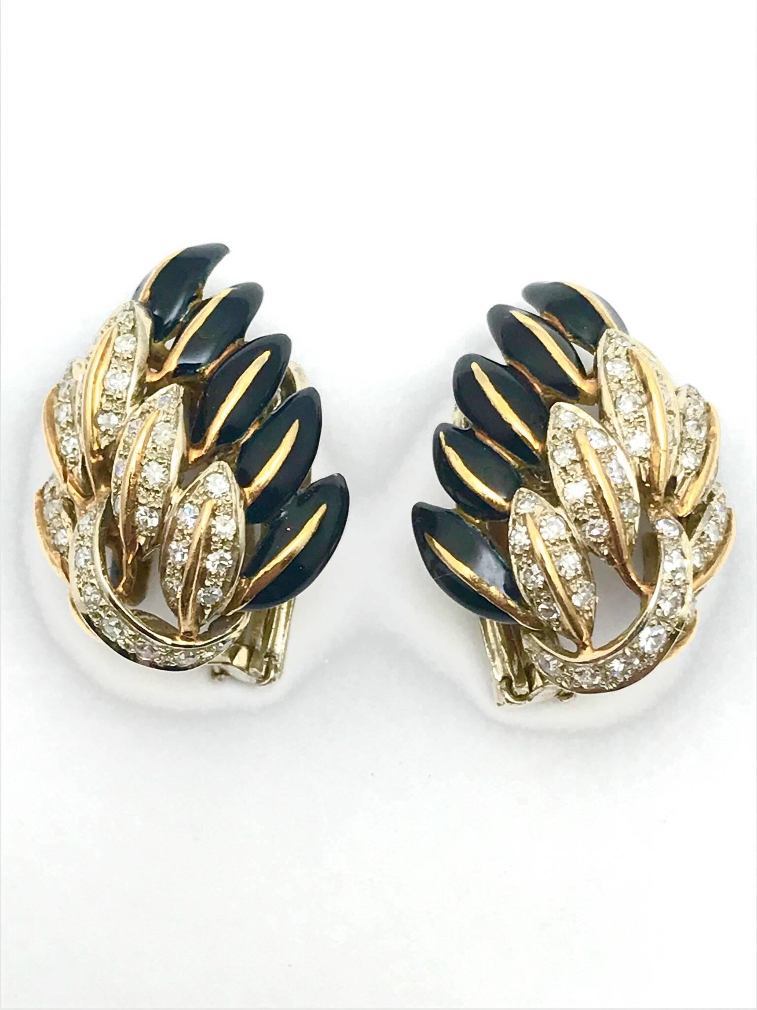 A pair of black enamel and diamond 18 karat yellow and white gold clip earrings.  The earrings are designed as a group of feathers, with diamonds set in white gold, layered on top of the black enamel feathers.  There are 90 round single cut diamonds