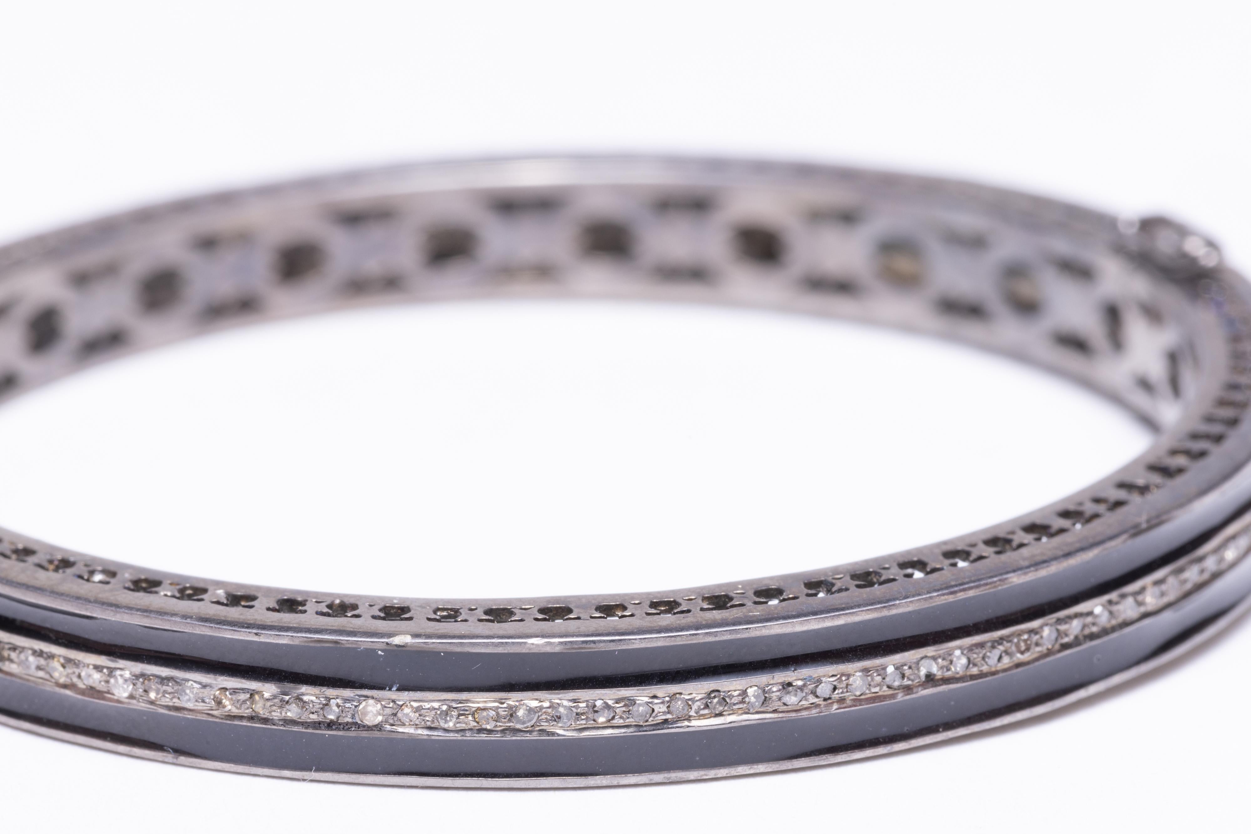 A black enamel and sterling silver bangle bracelet with a line of round, brilliant cut diamonds set down the middle.  Inside circumference is 7