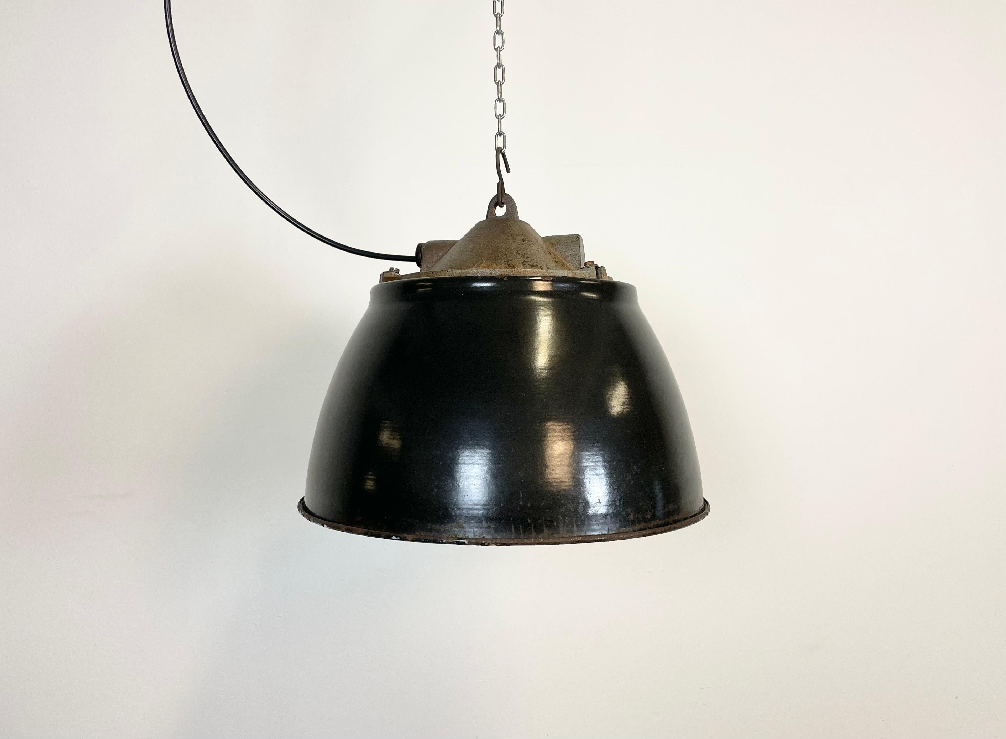 Industrial factory pendant lamp in cast iron made in former Czechoslovakia during the 1950s. It features a black metal enamel shade with white enamel interior, a striped glass and an iron cage. The porcelain socket requires E 27 light bulbs. New