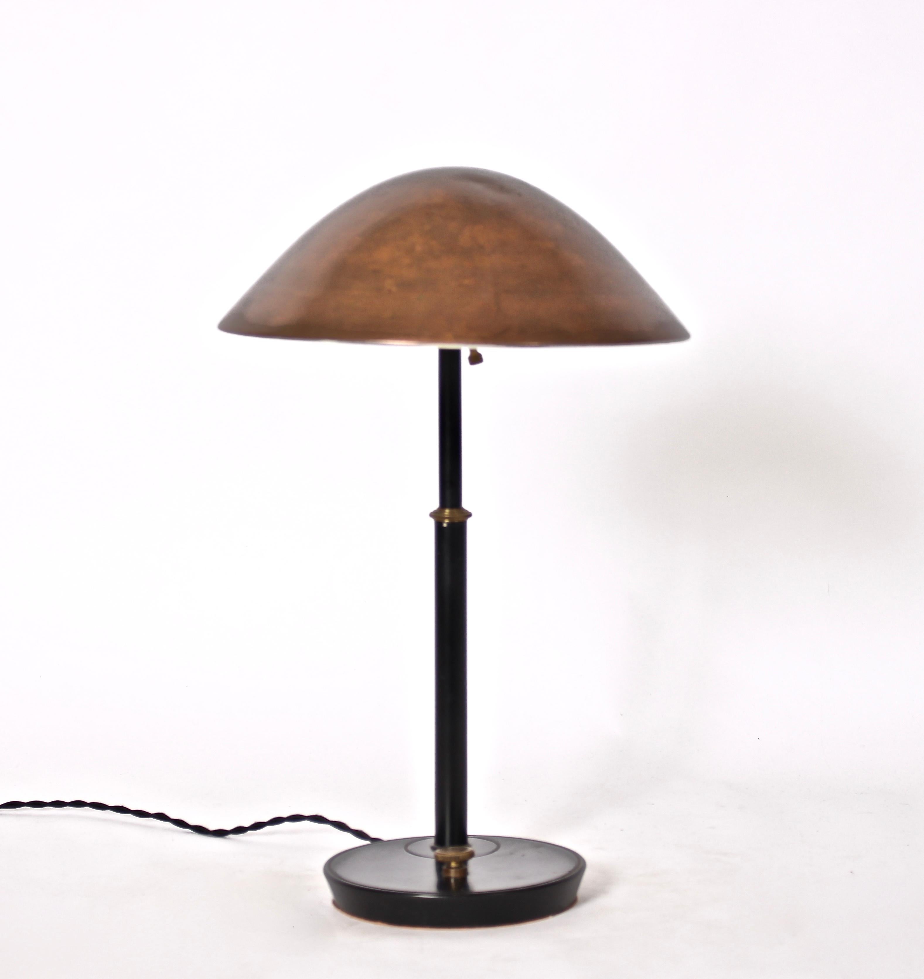 American mid century black enamel reading lamp with brass details and copper shade. Featuring a brass detailed black stem, round patinated copper saucer shade with off-white interior on round 7D weighted base. With hood and base switch. 