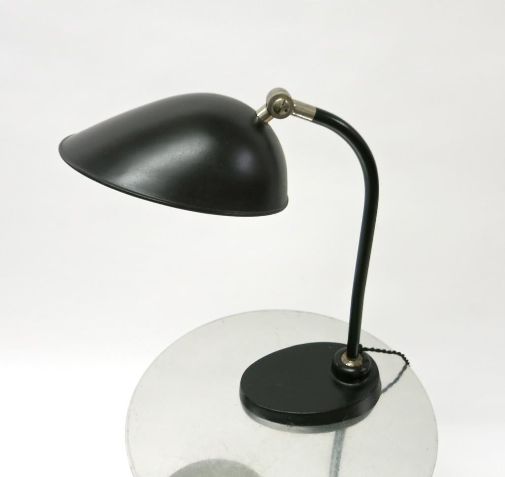 Table or desk lamp in black enameled metal with an ovoid shaped articulating shade, a tubular stem that connects the shade to the ball joint on the ovoid shaped base, allowing for backward and forward positioning, and nickel plated hardware.