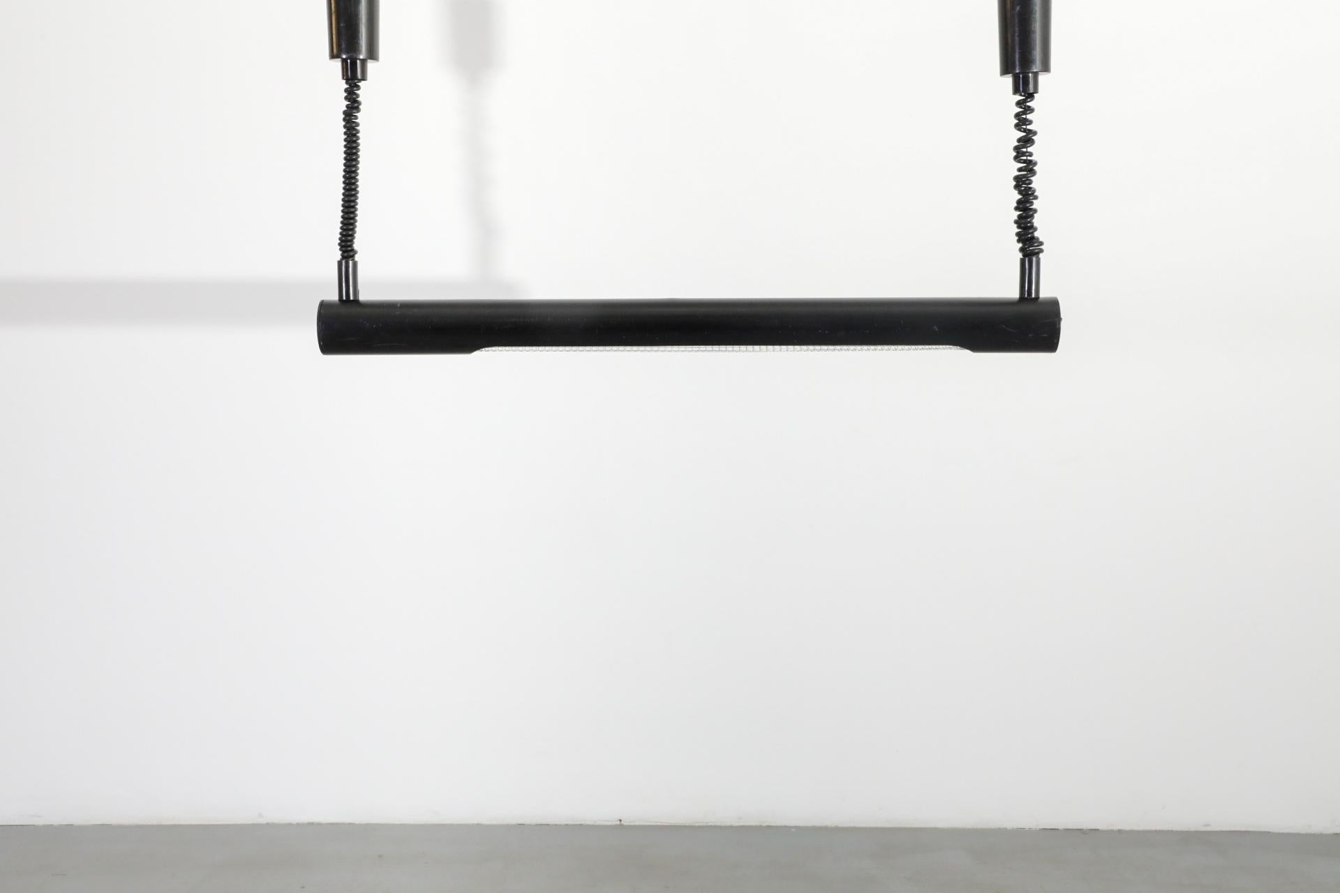 Lampada fluorescente tubolare lineare smaltata di nero di Massive nello stile di Anders Pehrson. Questa lampada è montata a incasso sul soffitto e un lato è cablato. Entrambi hanno un cavo telefonico retrattile con tettoie nere. In condizioni