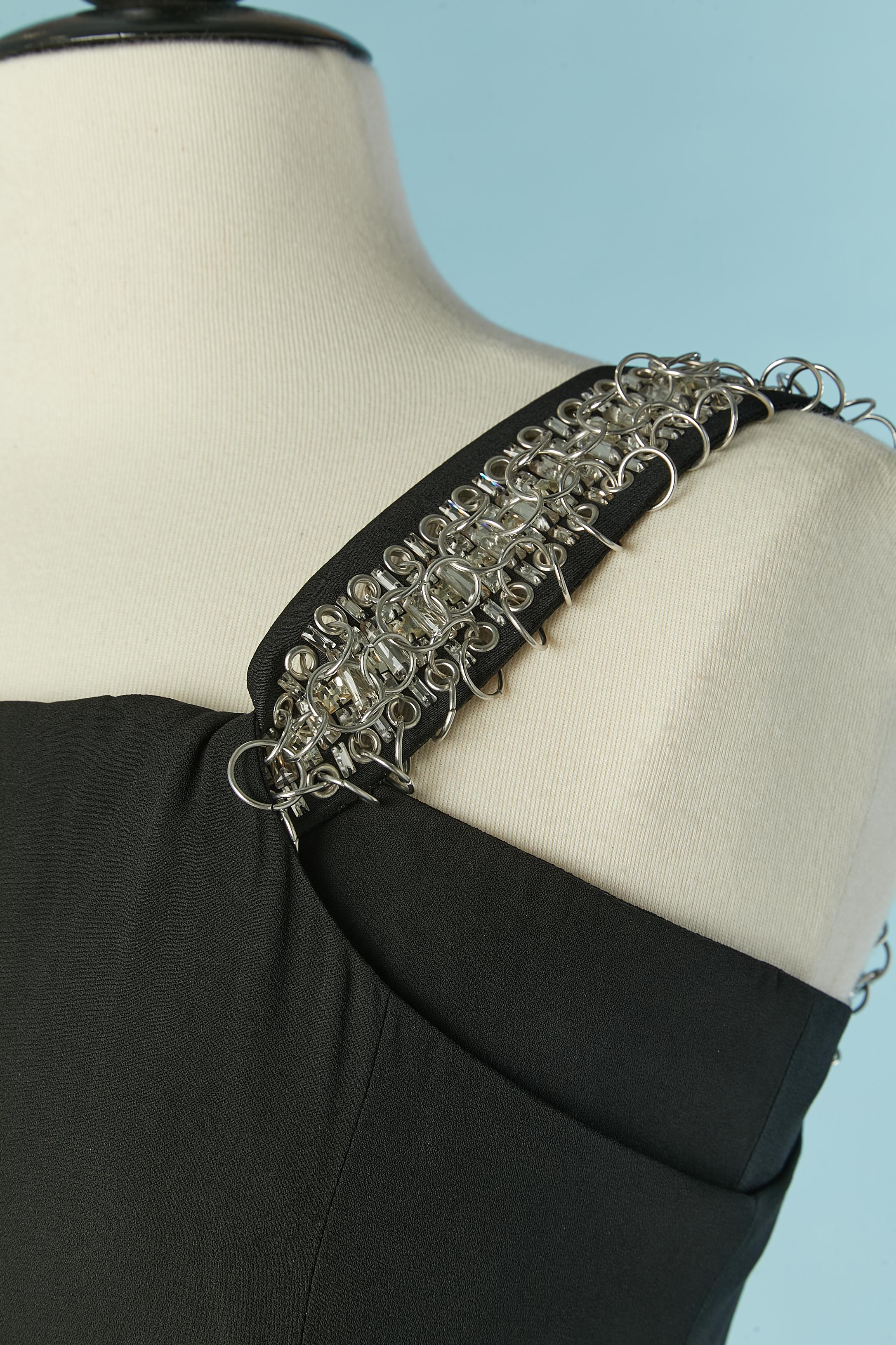Vestido de noche negro con anillos de metal plateado y strass 
 adorno en la bandolera. 
Composición del tejido principal: 58% rayón, 42% acetato. Bustier deshuesado en el interior del busto con cierre de corchetes en la parte central de la espalda.