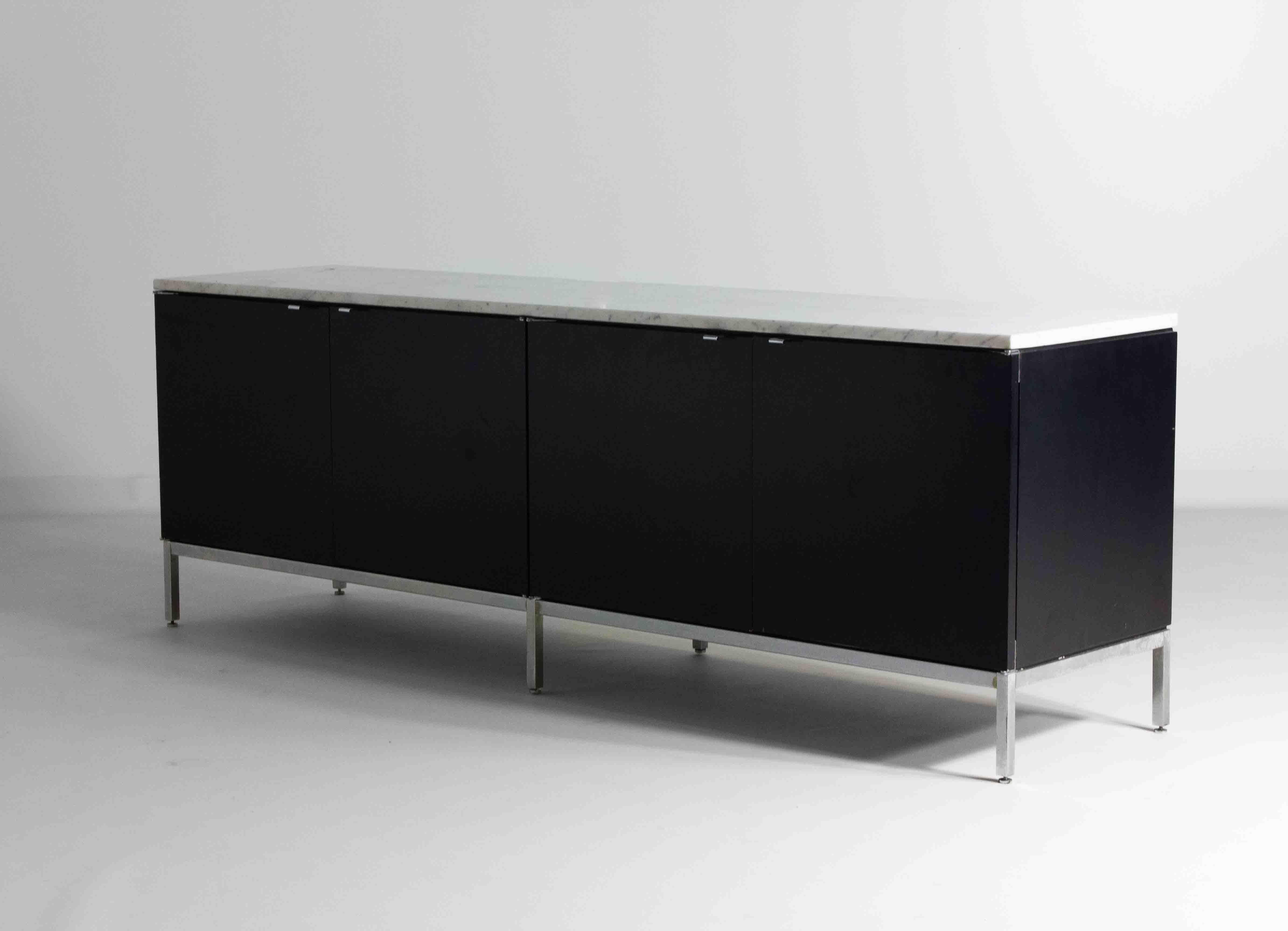 Mobile nero di Florence Knoll con base e maniglie cromate. Il legno nero intenso contrasta elegantemente con il piano in marmo bianco, accentuato da sottili venature grigie. Un'ampia scaffalatura può essere personalizzata senza costi aggiuntivi. Con
