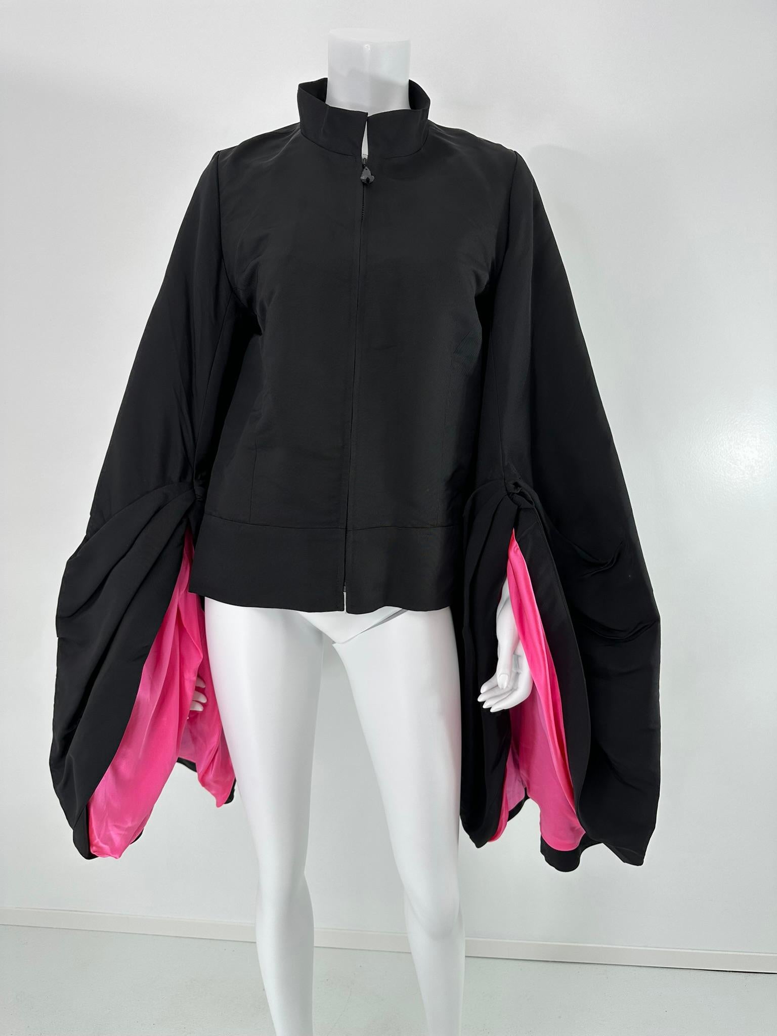 Giacca in faille nero e raso di seta rosa caldo, con zip sul davanti e maniche drappeggiate oversize. Questa giacca di grande effetto ha un colletto a fascia che si chiude sul davanti con una cerniera che ha un tiretto Jewell nero sfaccettato. Le