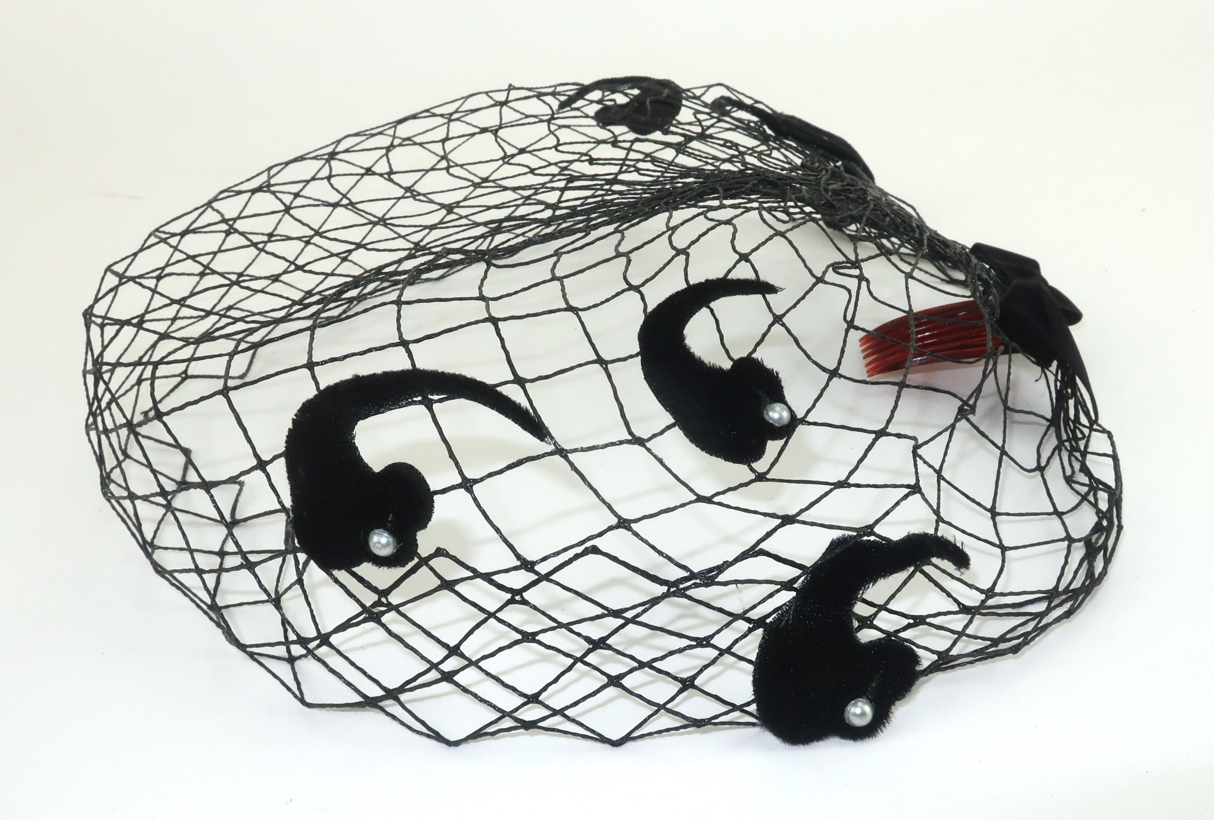 Schwarzer Netzschleier aus den 1950er Jahren, der allein oder in Kombination mit einem Hut getragen werden kann.  Der Fischnetzkörper hat eine steife Form, die am Rücken mit einer Schleife aus Samt gerafft und mit paisleyförmigen Samtverzierungen