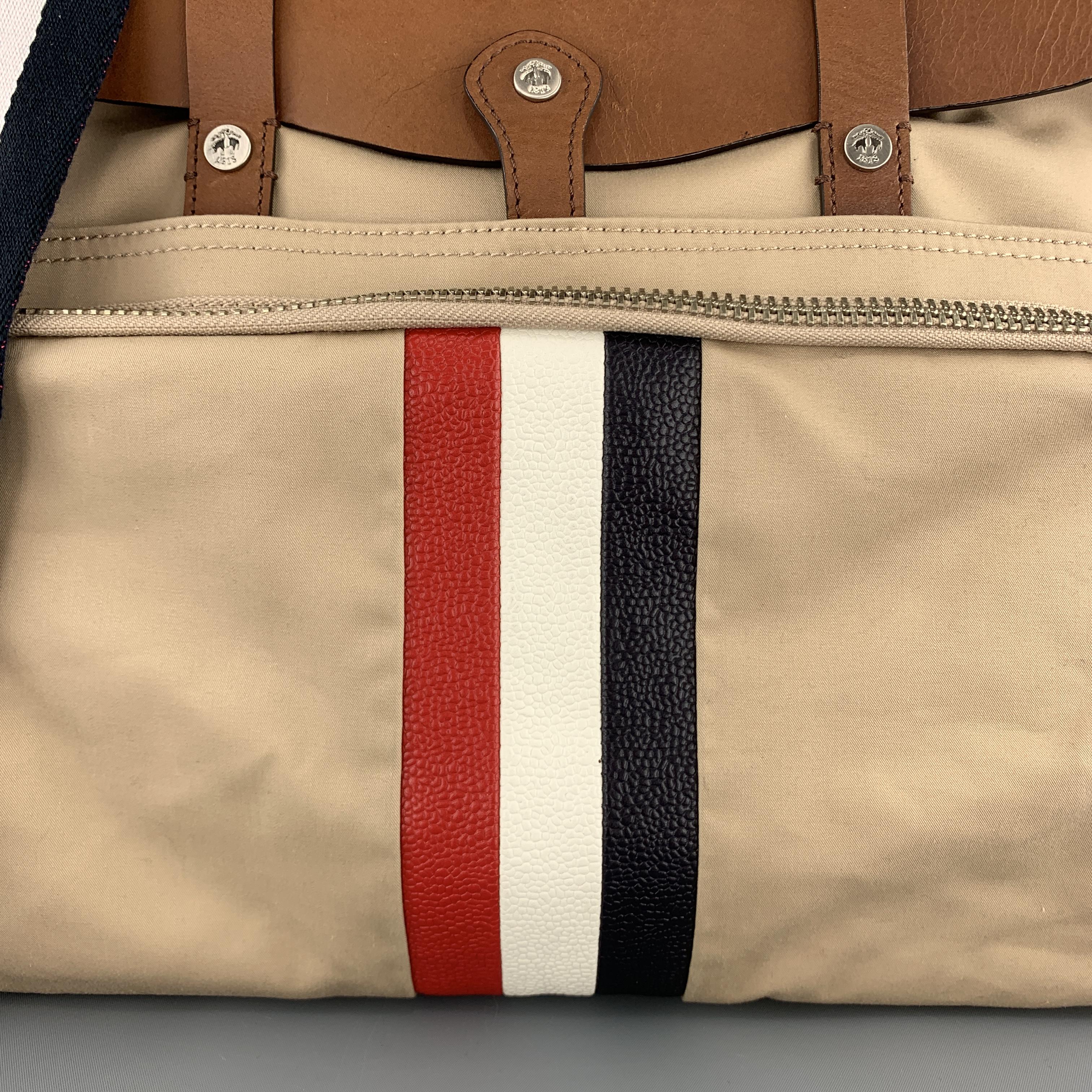 BLACK FLEECE by THOM BROWNE men's satchel bag comes in  khaki canvas with with a frontal zip pocket, tan leather flap top with double straps, top zip closure, back pocket, detachable webbing crossbody strap, and red, white, and navy blue pebbled