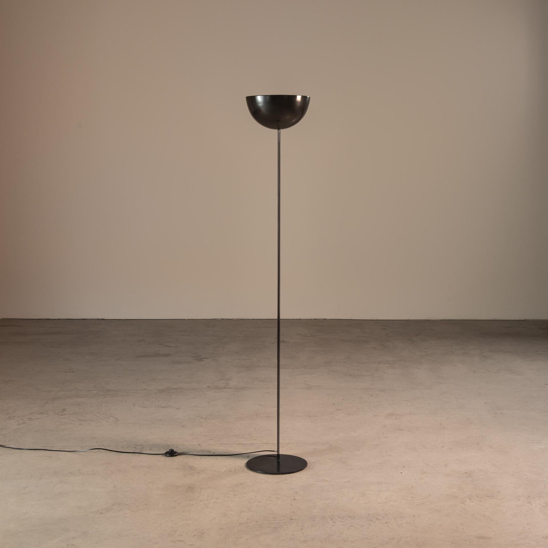 The black floor lamp is a mid-century modern design by Enrico Furio, created in the 1950s for his company Dominici. This particular lamp is recognized for its sleek design, featuring a polished, ebony-hued disc-shaped base and a slim, elongated