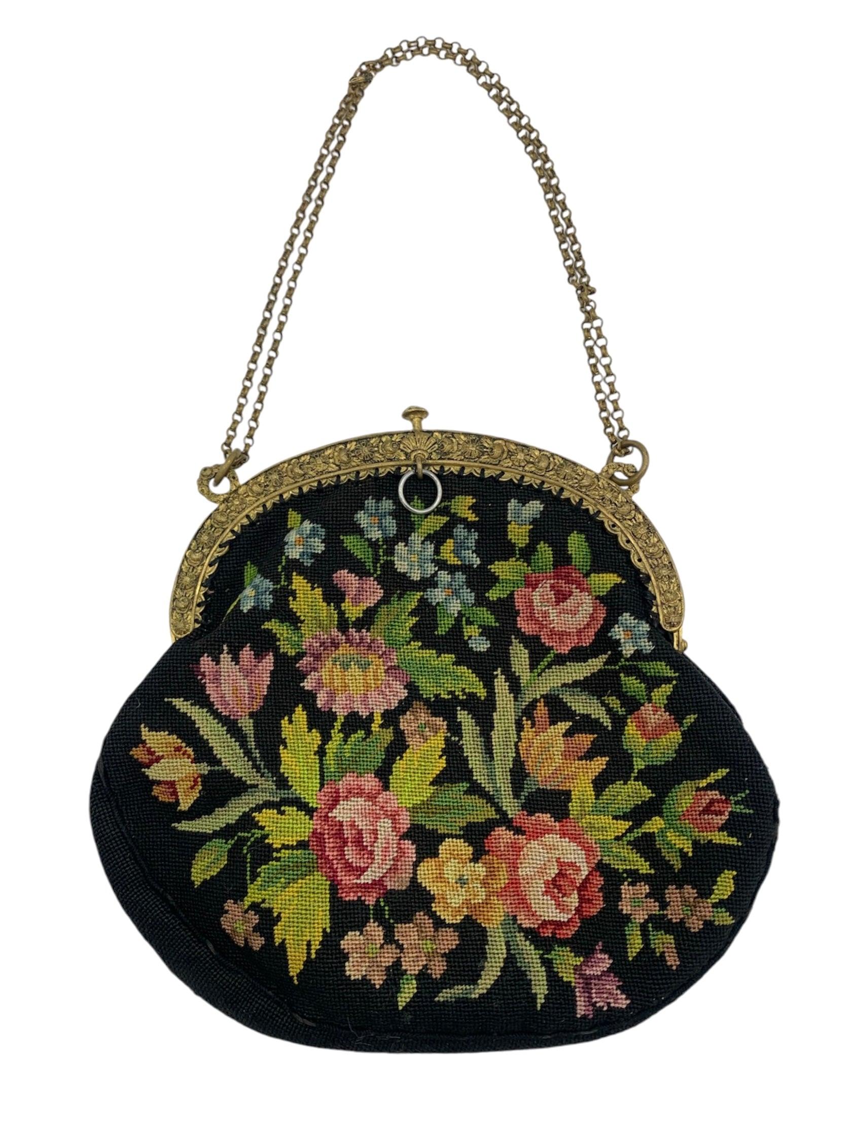 An incredibly sweet example 1920s petit point needle work. Jumbo floral motif across a black backdrop. Hammered gold-toned repoussé frame. Gold-toned adjustable double drop chain. Press and release closure at the top of the frame. Pink rayon lining