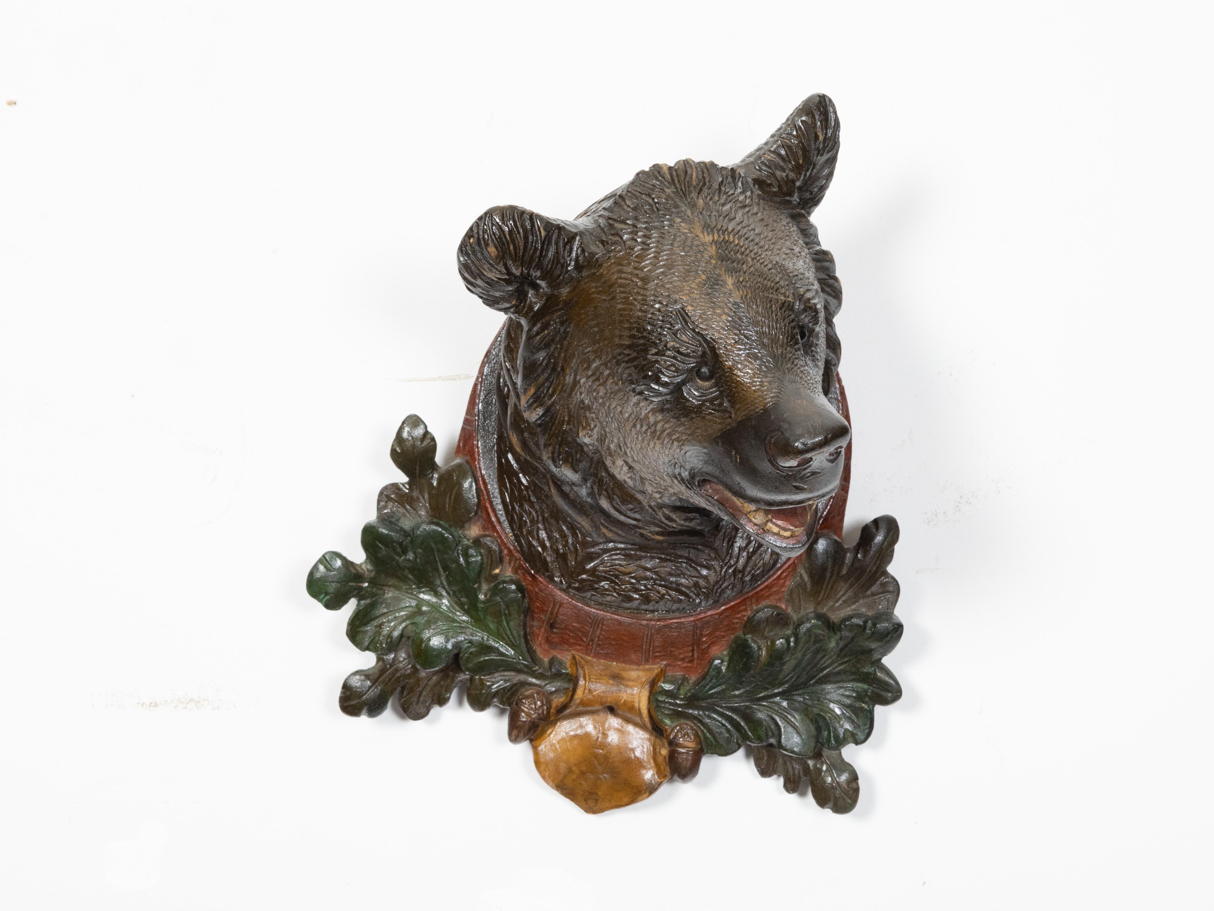 A black forest carved wooden bear head from the late 19th century, with oak leaves and green, yellow and red accents. Created during the last quarter of the 19th century, this Black Forest wall hanging sculpture depicts a brown bear's head springing