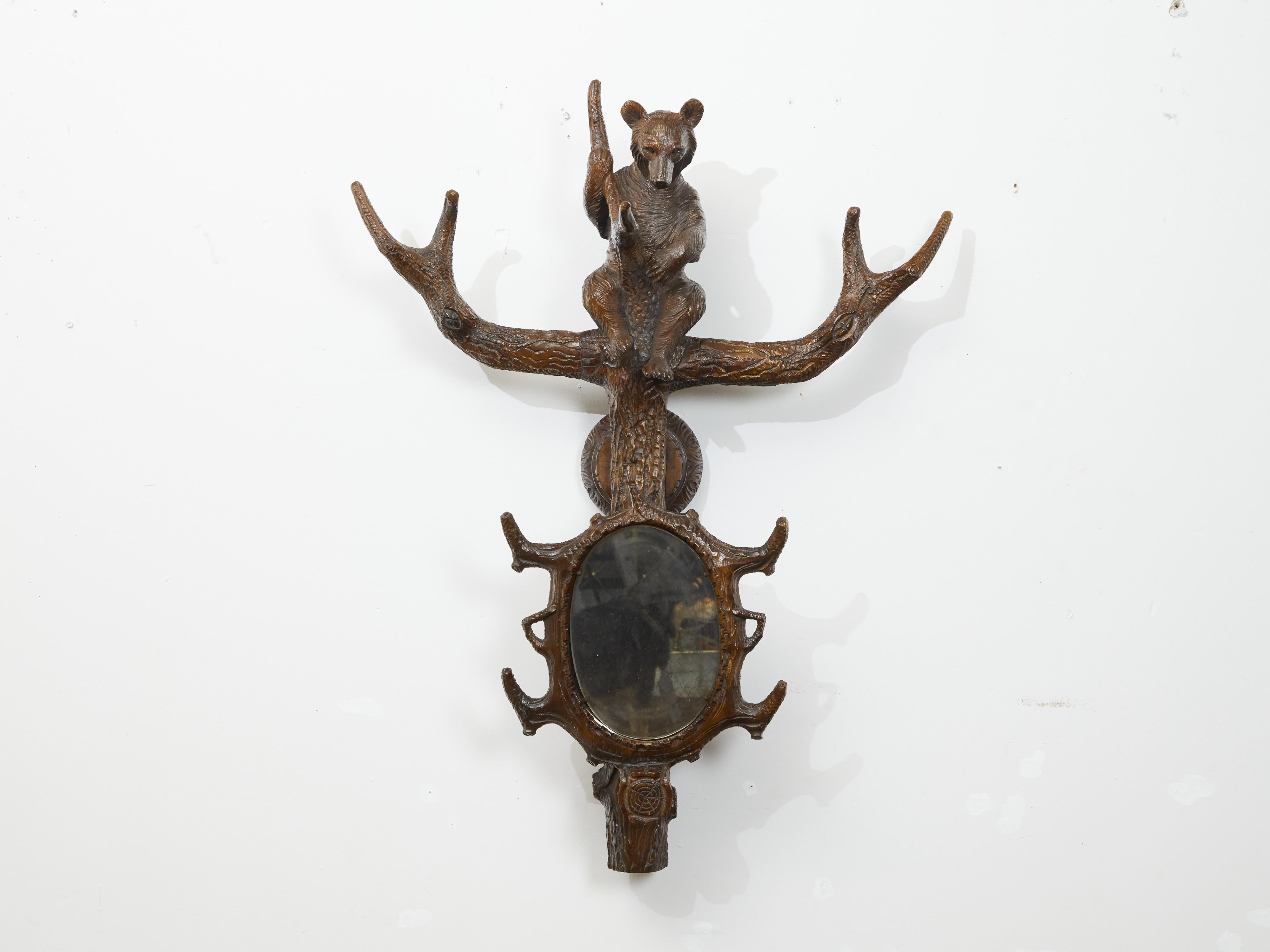 Adorno colgante de pared de madera tallada de la Black Forest de principios del siglo XX, con motivo de oso y espejo central. Creada durante los primeros años del siglo XX, esta pieza de la Black Forest capta nuestra atención por su encantadora
