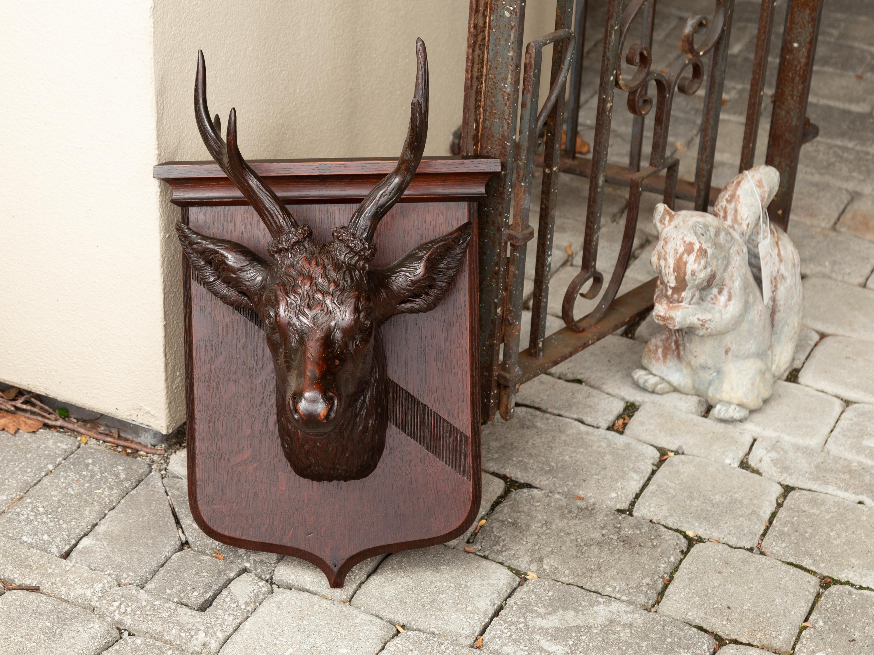 A Swiss Black Forest hand carved wooden buck head wall sculpture from the turn of the century, with shield plate. Born in the early years of the 20th century, this exquisite wall sculpture depicts a carved buck mounted on a shield-shaped plate. Our
