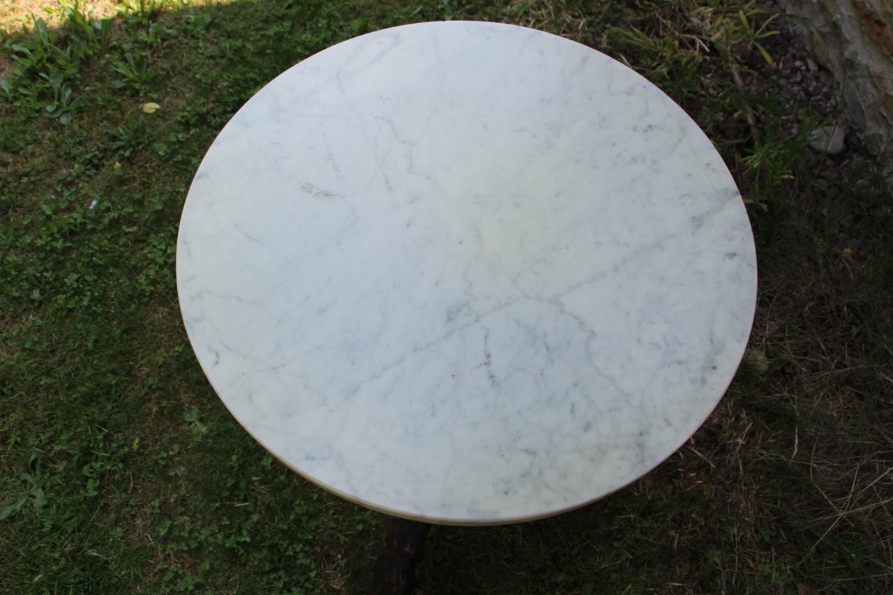 Charming pedestal table with a circular white marble top resting on a central carved wooden base with a naturalistic decoration imitating intertwined branches. The central shaft has finely executed carving work, resting on a tripod formed by curved