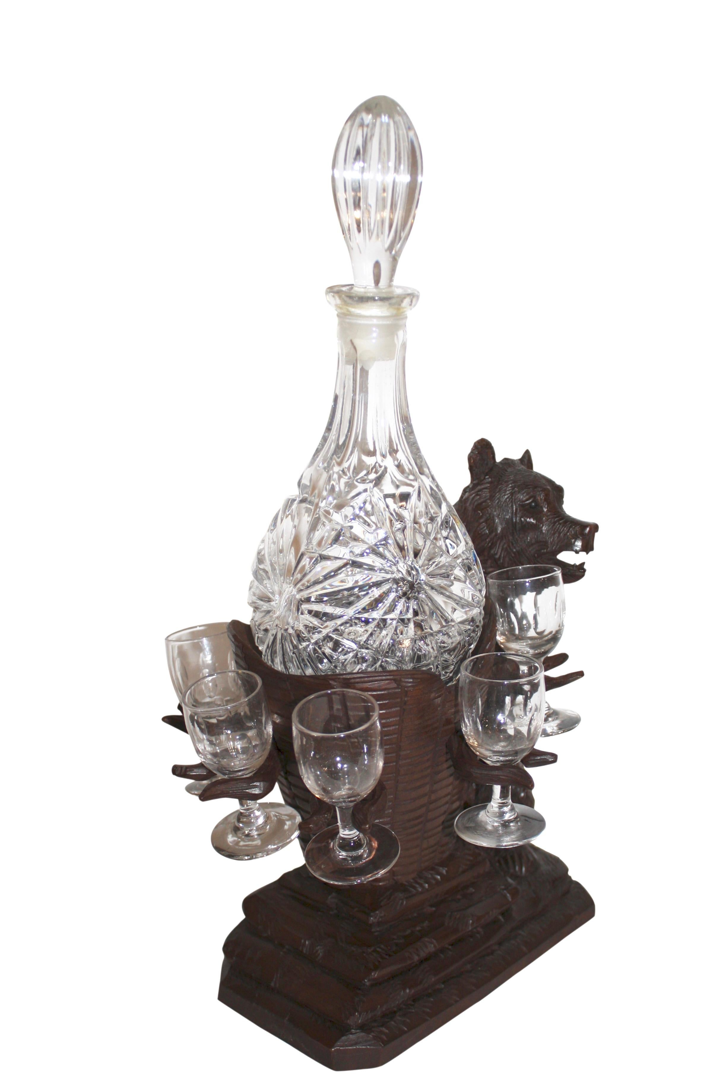 Looking very pleased with himself, this whimsical, Black Forest bear carries a wicker basket with a decanter larger than he is. Six stemmed glasses are suspended from the basket.
 