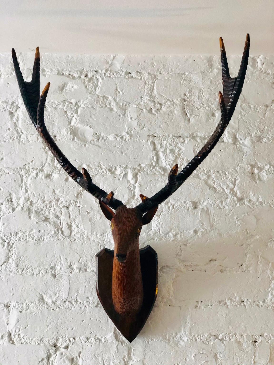 Black Forest carved deer or stag head & antlers mounted on shield plaque, Germany, 1900

Early 20th century Black Forest carved wood stag head with antlers. The antlers and head are all hand carved, mounted onto a shield shape plaque.
The amber