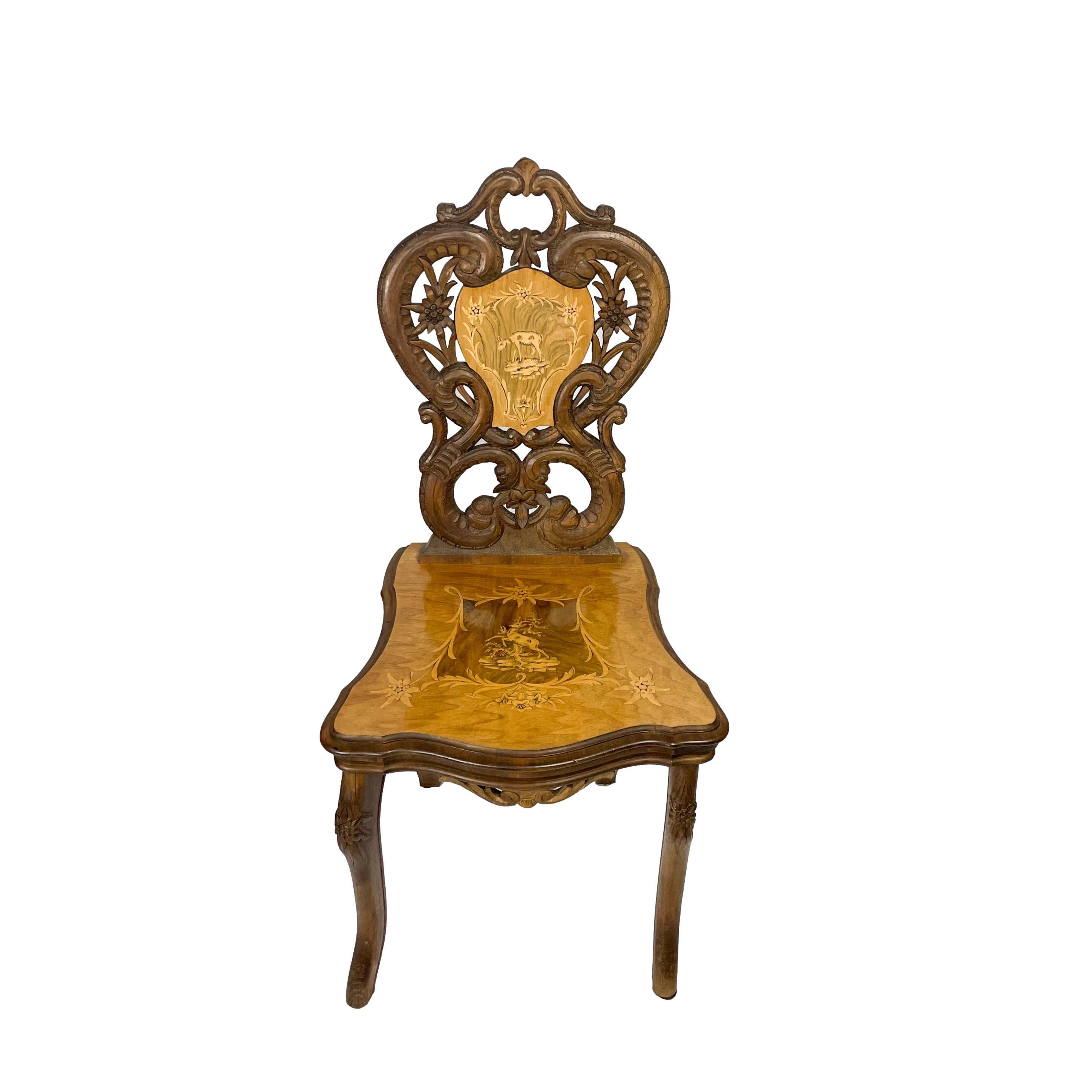A Black Forest Carved Walnut Chair, the seat and seatback with intricately inlaid cartouches each depicting an alpine chamois, with carved edelweiss and leaves, with the working music box mechanism under the seat, Brienz, Switzerland, ca. 1900. 
