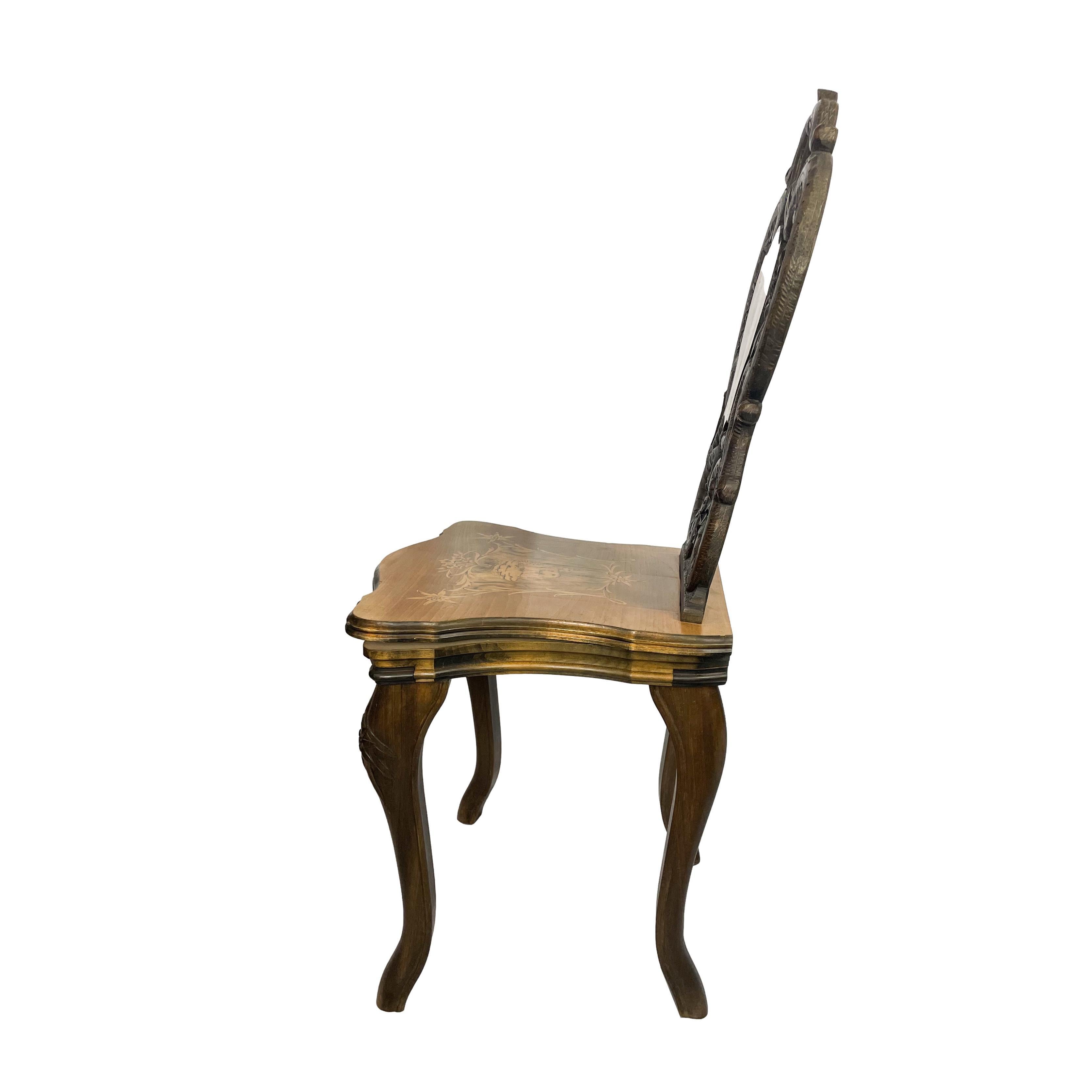 A black forest carved walnut chair, the seat and seatback with intricately inlaid cartouches each depicting an alpine chamois, with carved edelweiss and leaves, with the working music box mechanism under the seat, Brienz, Switzerland, ca. 1900. 
