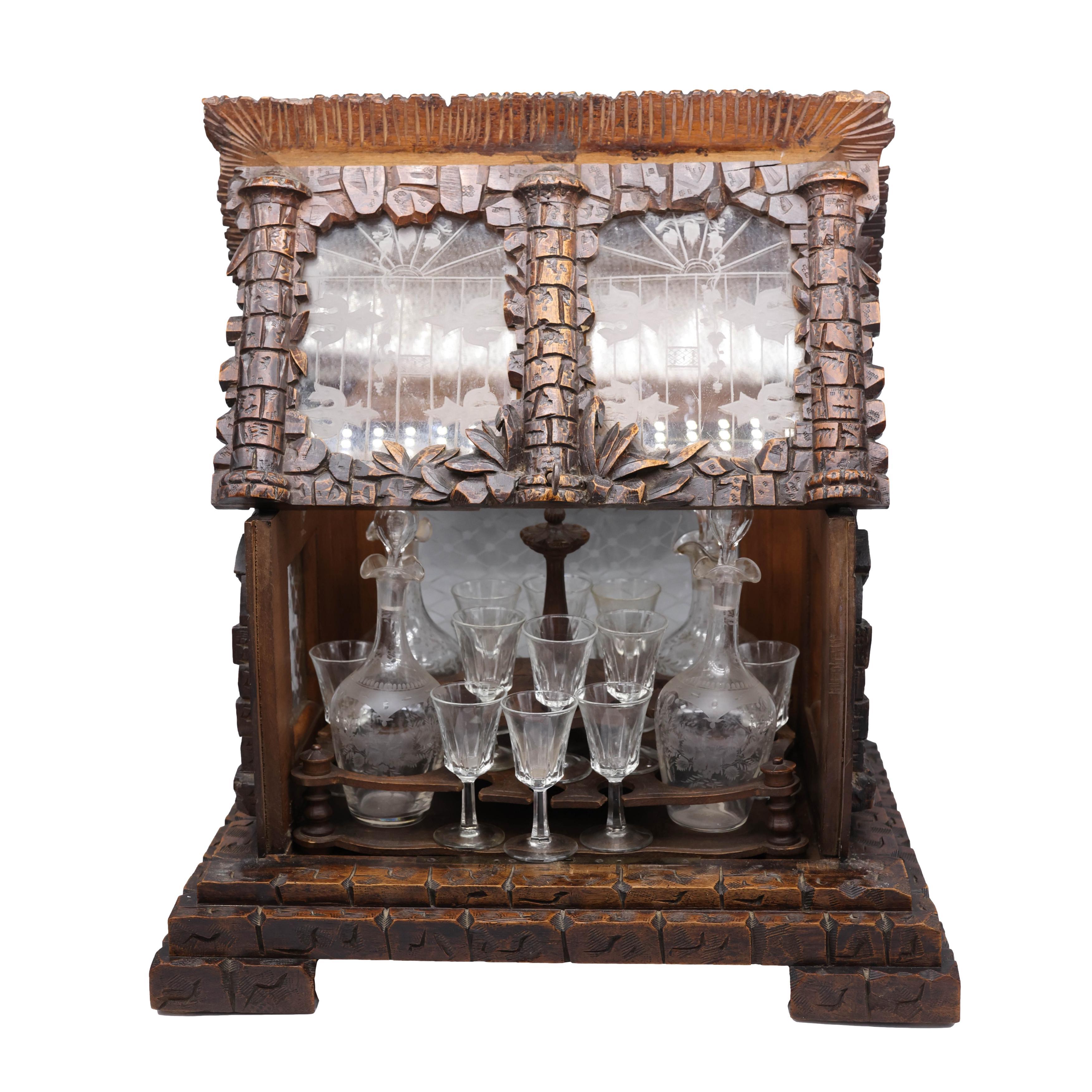 Exceptional black forest Tantalus set, the box hand-carved in the form of a house with individually carved stones, etched glass leaded windows, and thatched roof, surmounted by a carved hunting dog, with hinged front and top, the fitted interior