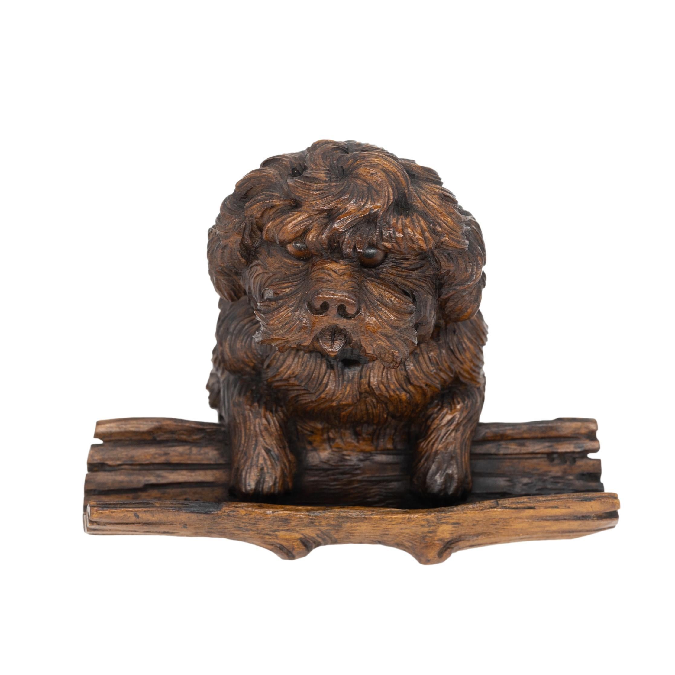 Black Forest Breinzware Inkwell, carved as begging terrier with tongue protruding, with inset glass eyes, the hinged head concealing a glass inkwell, the dogs front paws mounted on a naturalistically carved hollowed tree forming the pen tray,