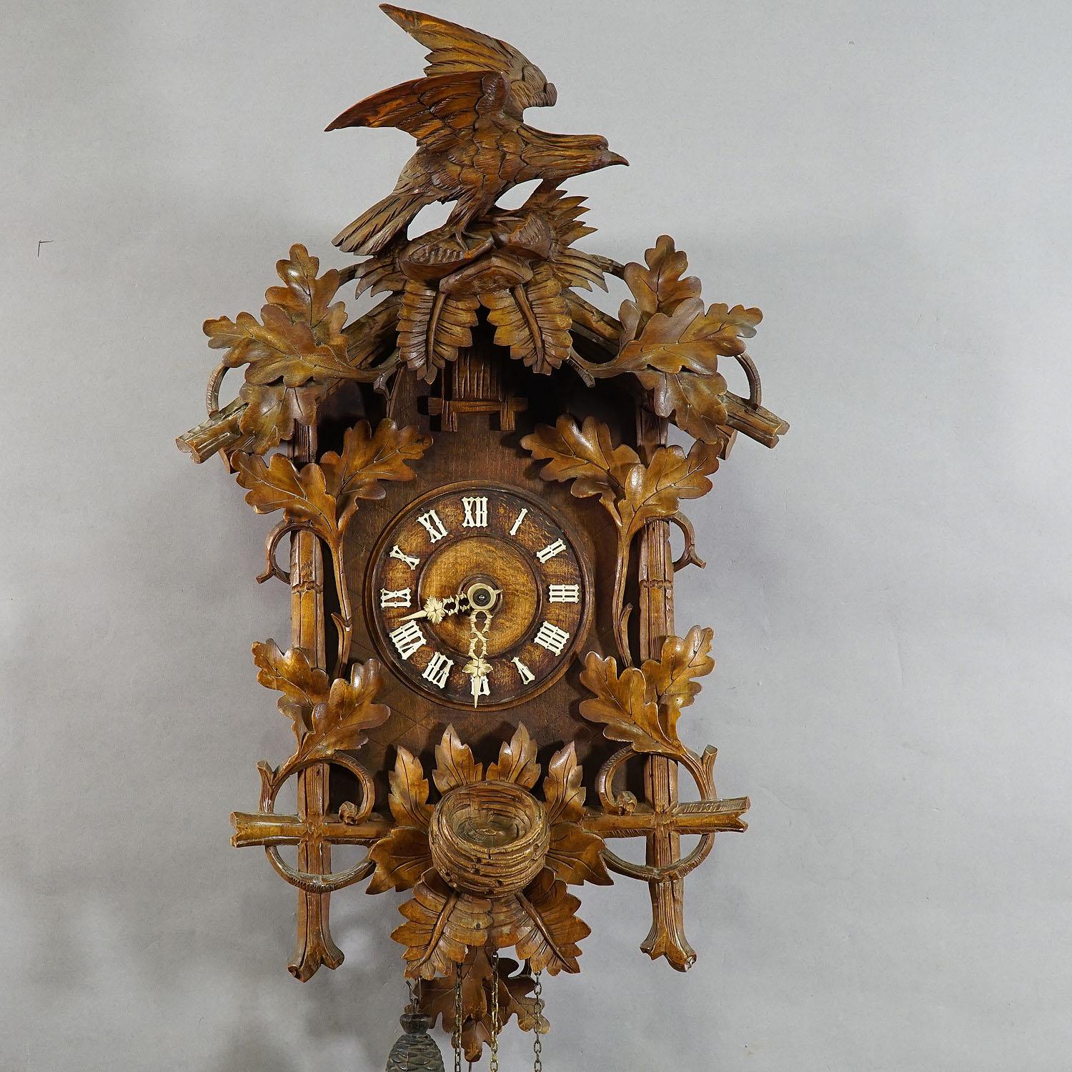 A detailed hand carved wooden cuckoo clock, decorated with oak leaves, birds nest and a large bird on top. Black Forest, Germany, circa 1900. Clockwork in working condition, overworked by a clockmaker.

Measures: Width 14.96