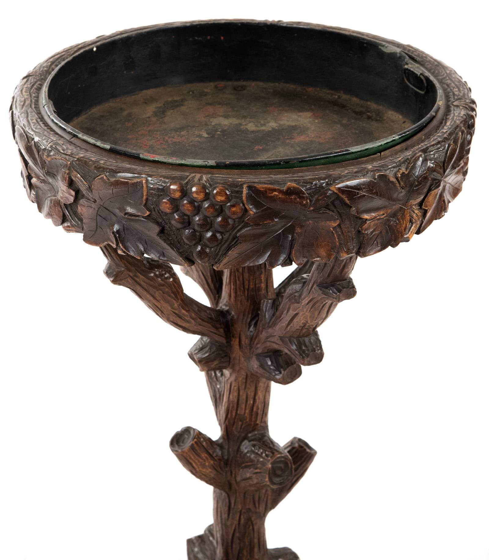 A 19th century black forest stand with a round top, its edges carved in relief with grapes and grape leaves and inset with a round metal dish, all raised on arms, stem and legs carved to represent wooden branches. Measures: 36 x 41 inches.