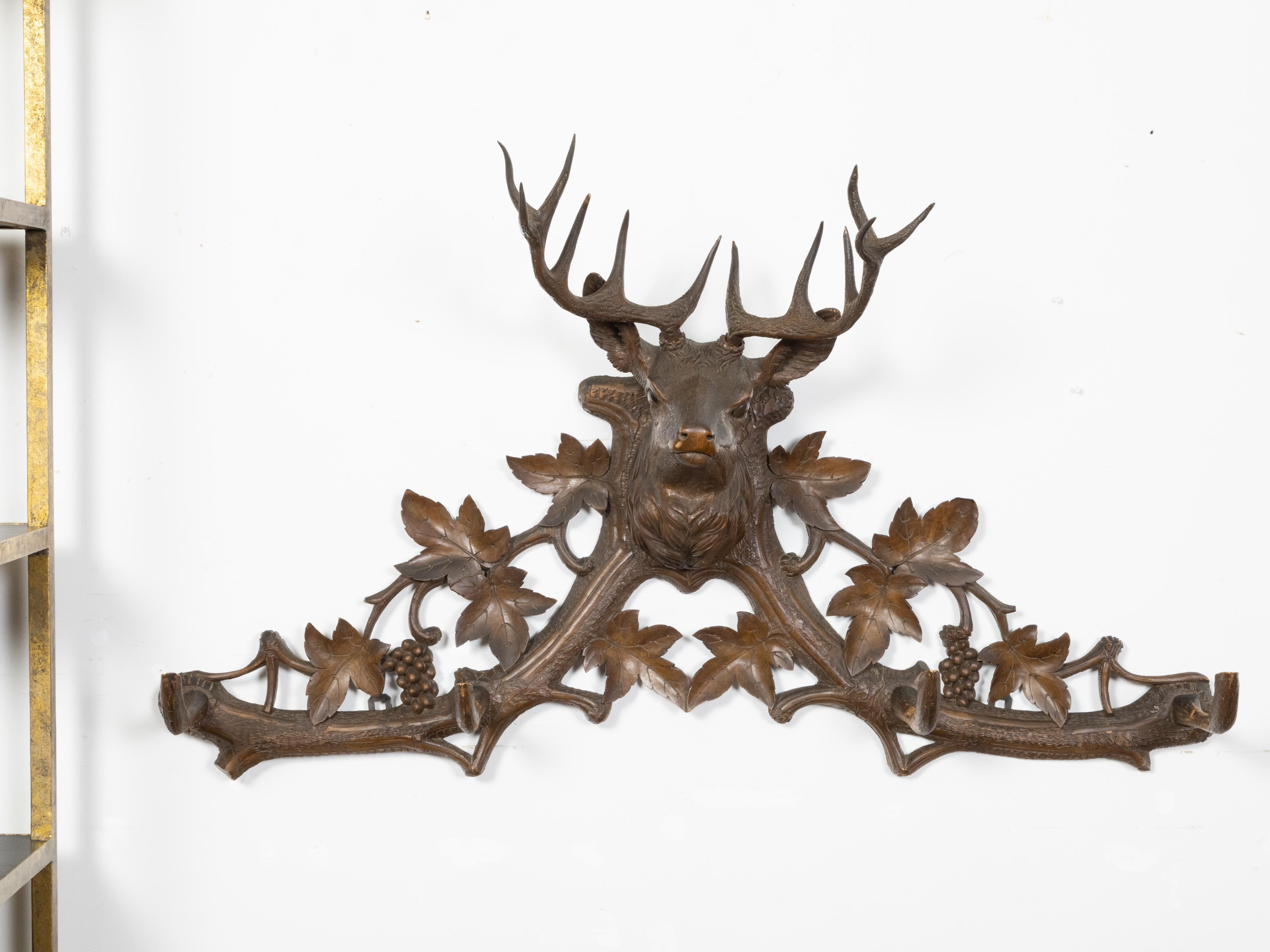 A Swiss Black Forest coat hanger from the early 20th century depicting a hand-carved stag head and grapevines. Created in Switzerland during the Turn of the Century (19th to 20th), this Black Forest coat hanger attracts our attention with its