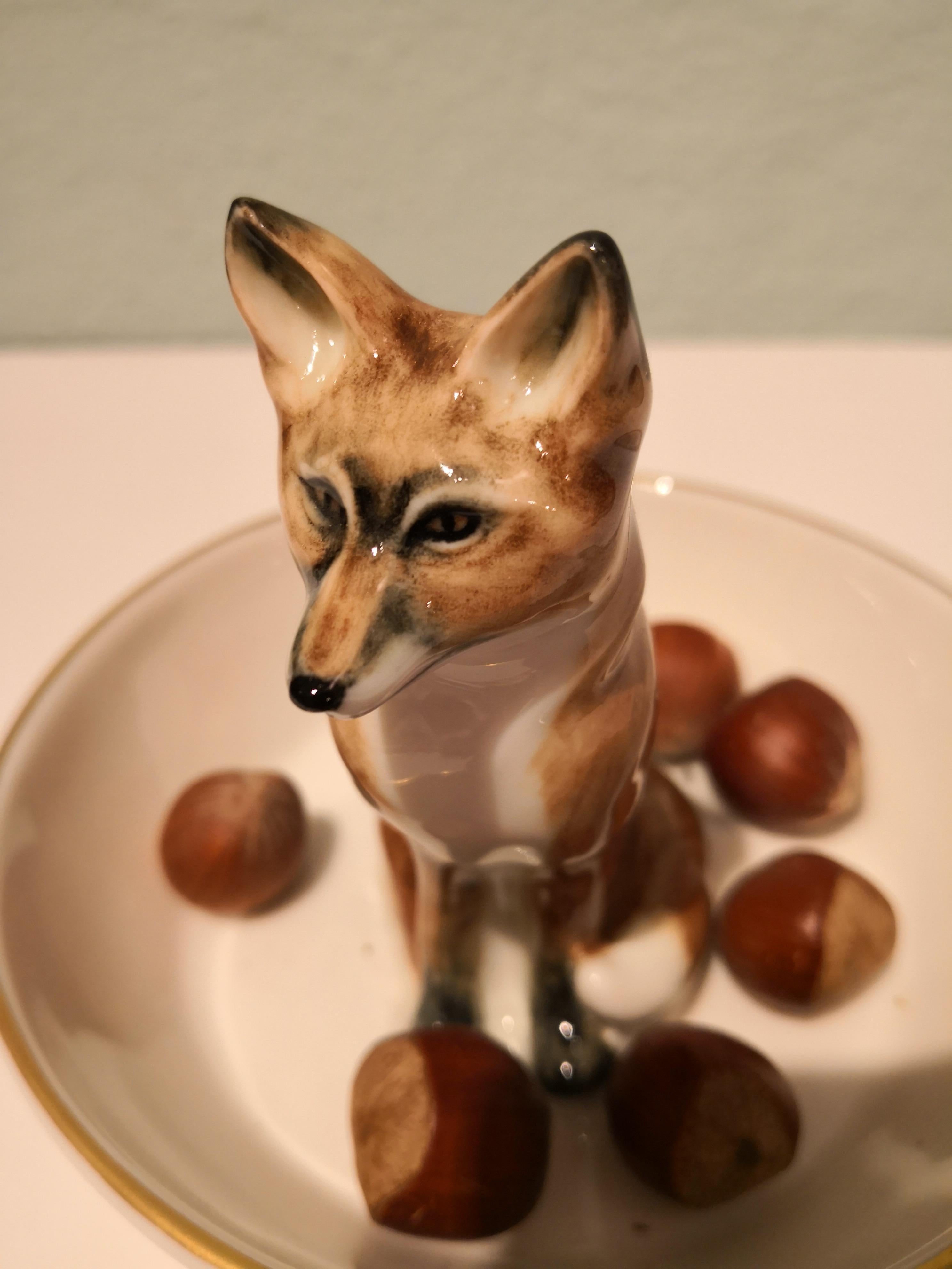 Bol en porcelaine entièrement fabriqué à la main avec une figure de renard naturaliste peinte dans des couleurs brunes. Le renard est assis au milieu du bol pour décorer les noix ou les sucreries autour d'un style d'intérieur de forêt noire. Il est