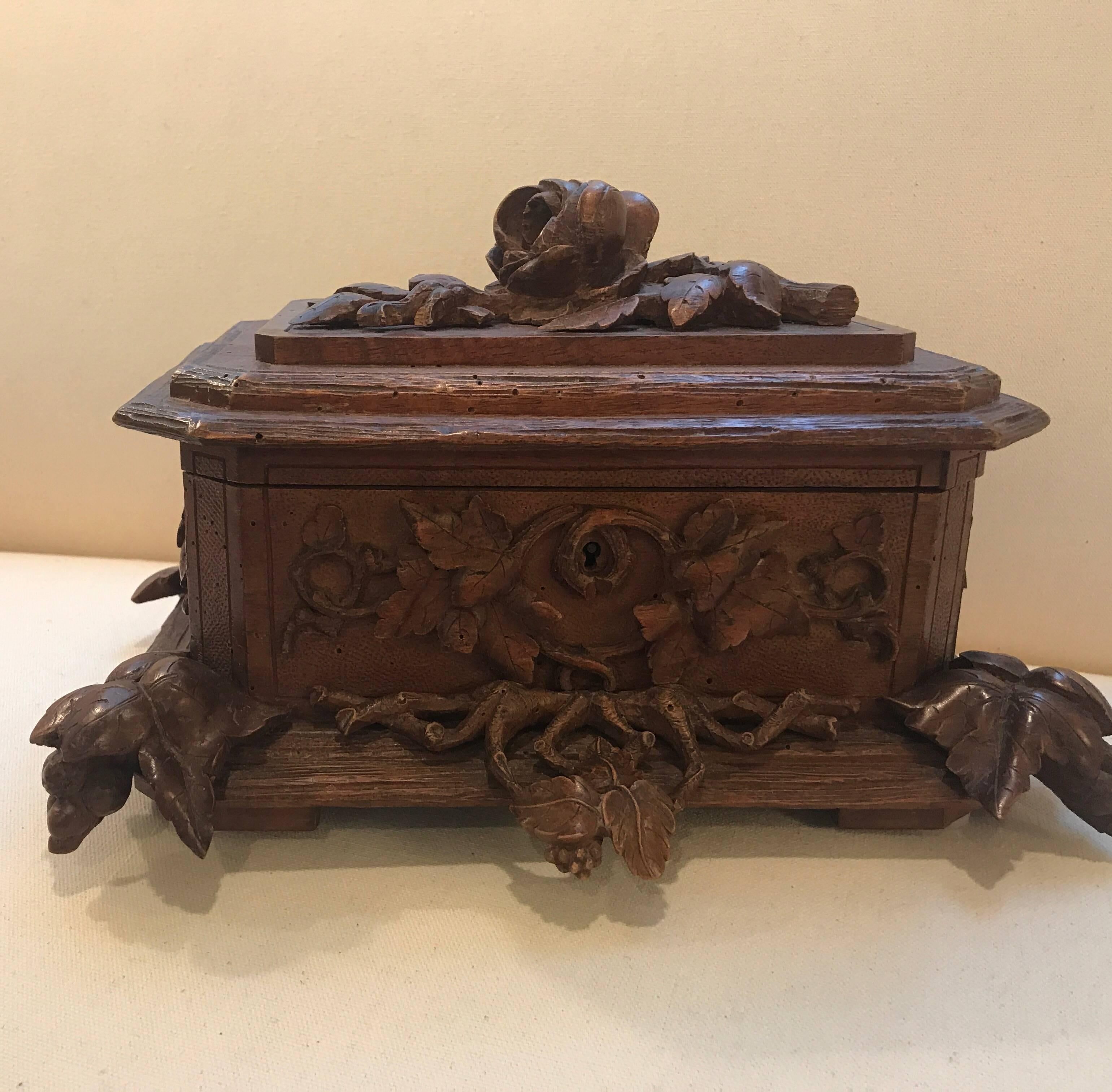 Expertly hand carved Swiss Black Forest hand carved table box. The hinged lid with floral and vine decoration over a carved bottom with ivy motif feet.