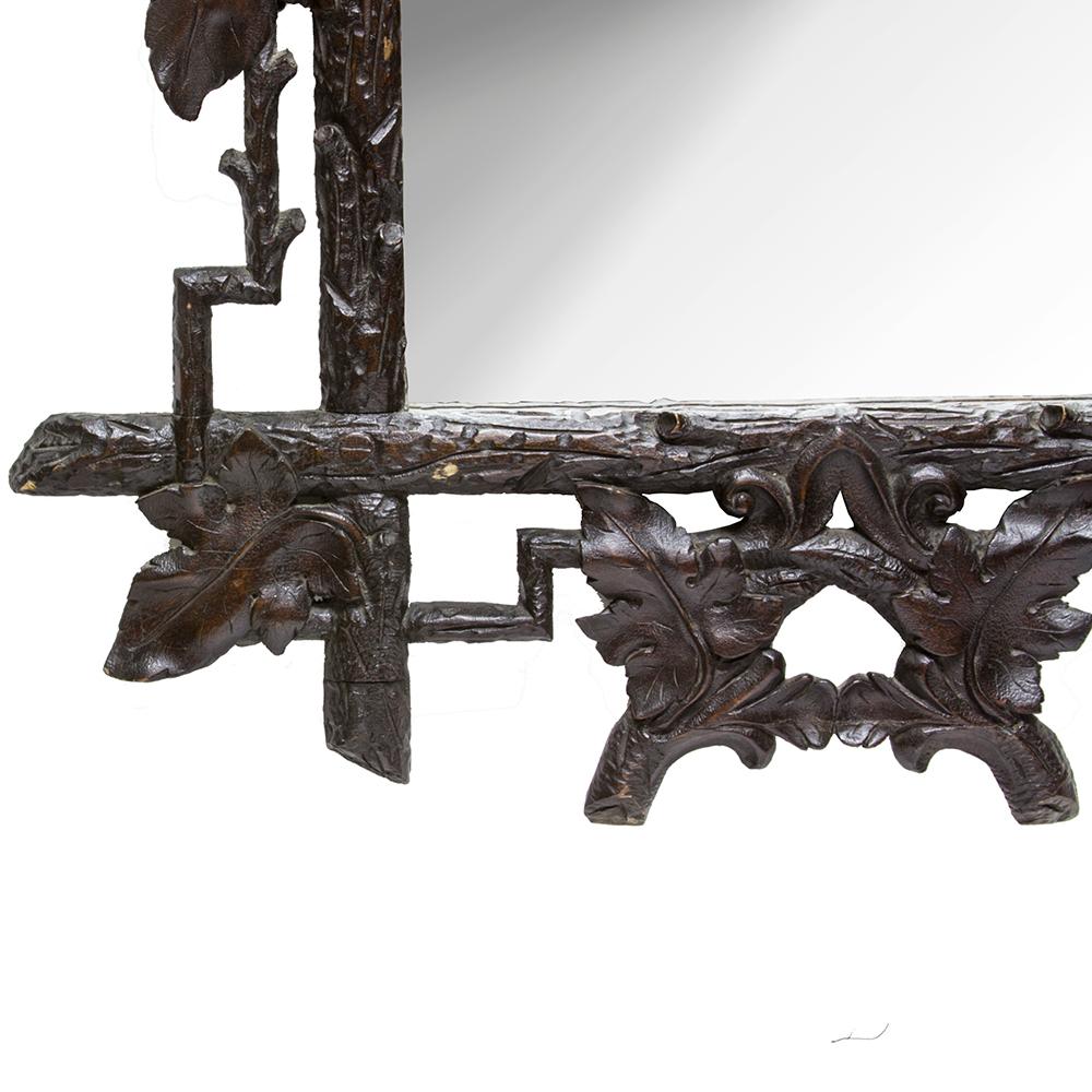 Rustic logs and grape vines adorn this whimsical Black Forest mirror. The darkened patina and well-executed carving of this handsome mirror make it a fine example of the Black Forest style. Late 19th century, mirror glass has been replaced.