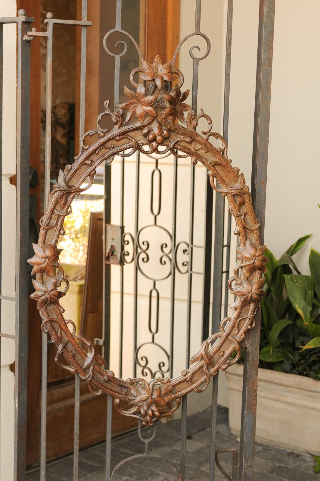 A Black Forest hand carved oak wall mirror from the early 20th century, with edelweiss flower decor. Born in the early 1900s, this exquisite oval wall mirror features an intricate frame, hand carved with delicate edelweiss flowers surrounded by