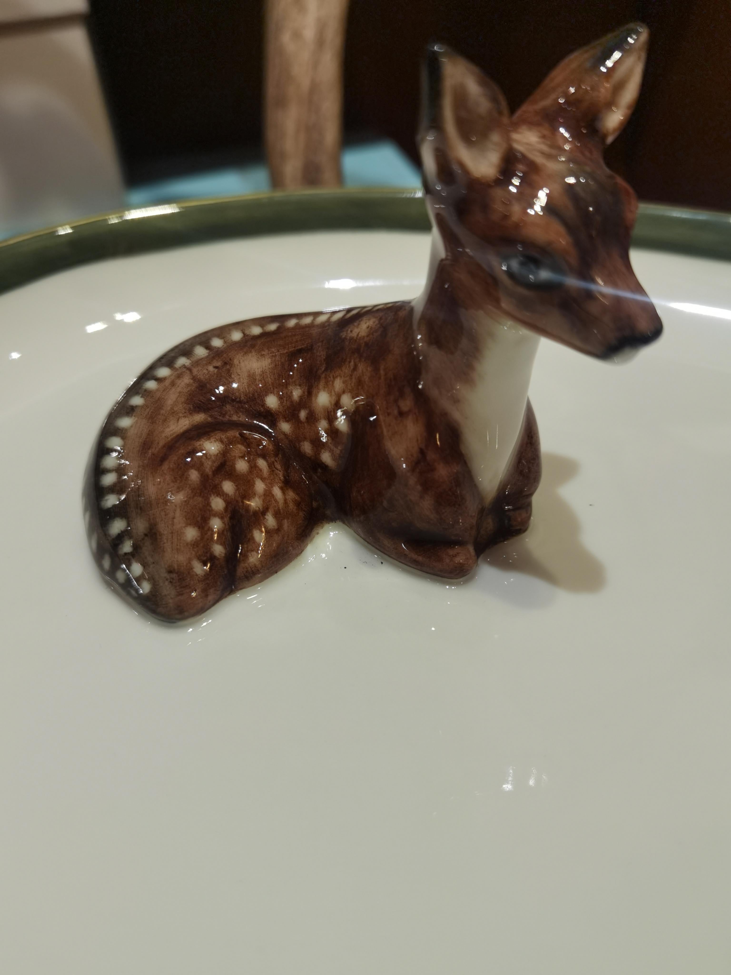 Completely handmade and hands-free painted large oval porcelain plate in Black Forest style. A natural molded porcelain bambi figure is sitting left hand and three pines are fixed on the porcelain plate. One pine is gilded in 24 carat gold. The