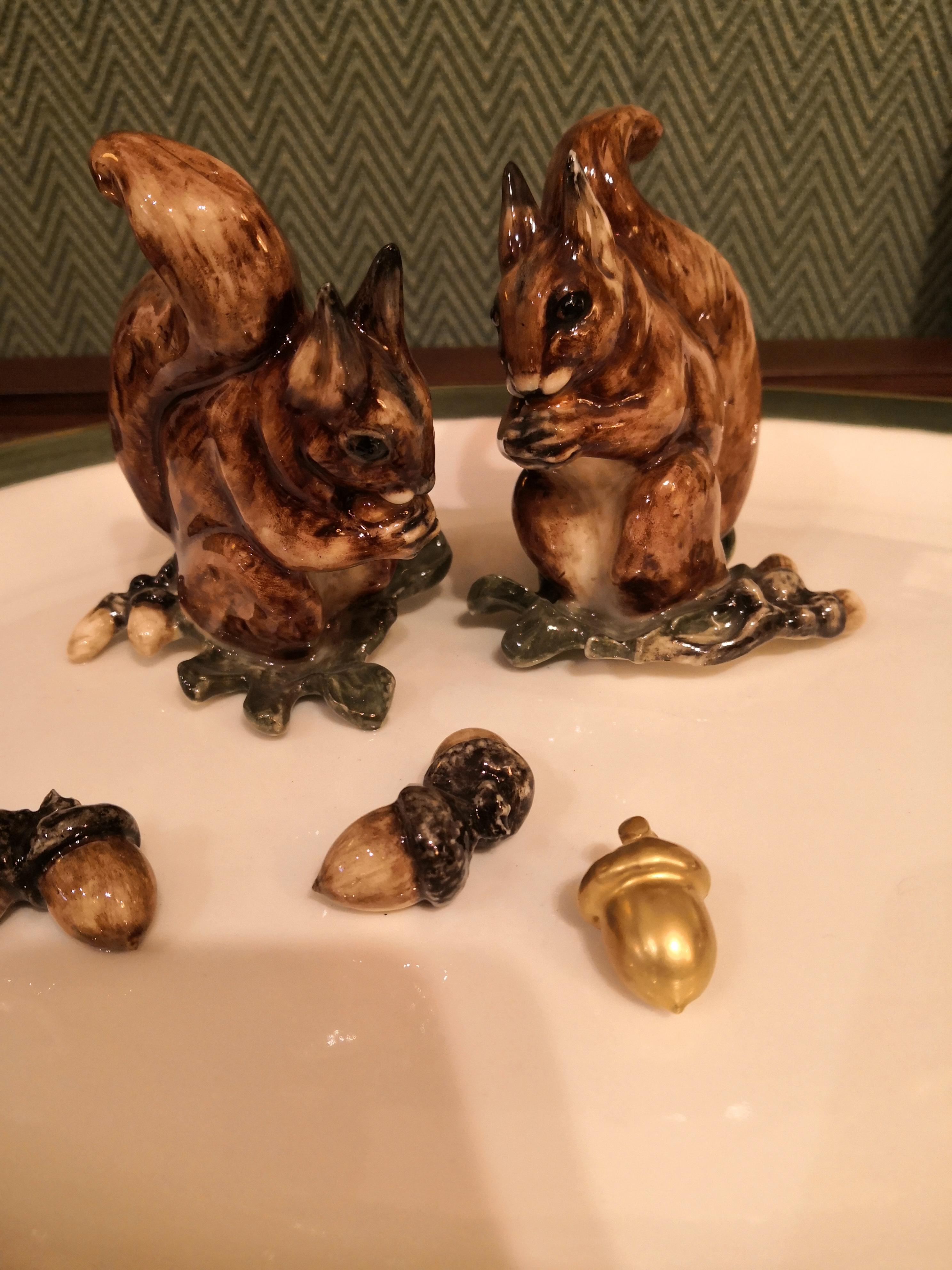 Completely handmade and hands-free painted large oval porcelain plate. Two natural molded porcelain squirrel figures sitting on oak leaves and oaks fixed on the porcelain plate. The plate is painted with a green rim and framed with a 24-carat gold