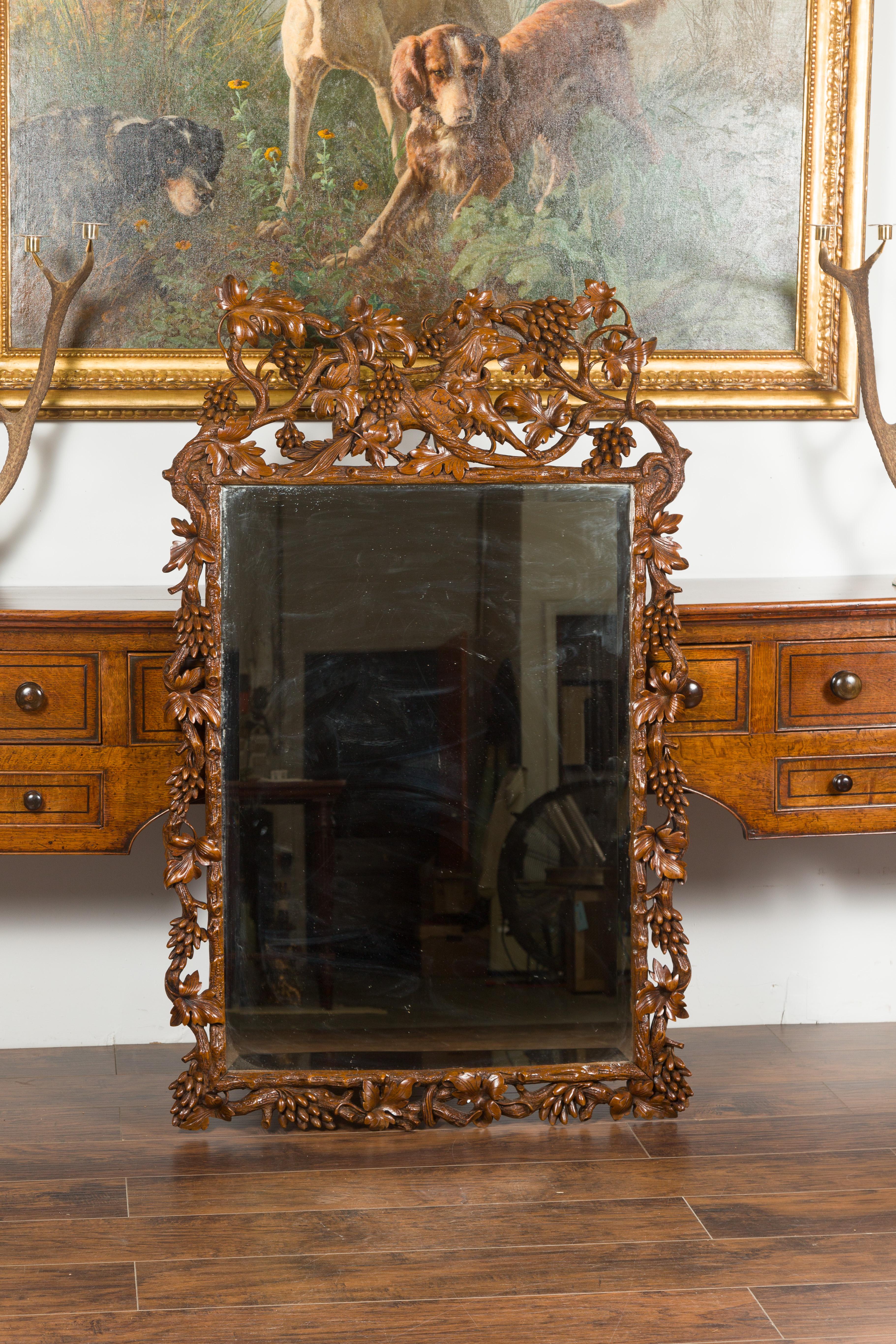 A Swiss Black Forest period wooden mirror from the early 20th century, with carved dog, foliage and fruits. Hand carved during the early years of the 20th century, this Black Forest mirror captures our attention with its skillfully carved crest