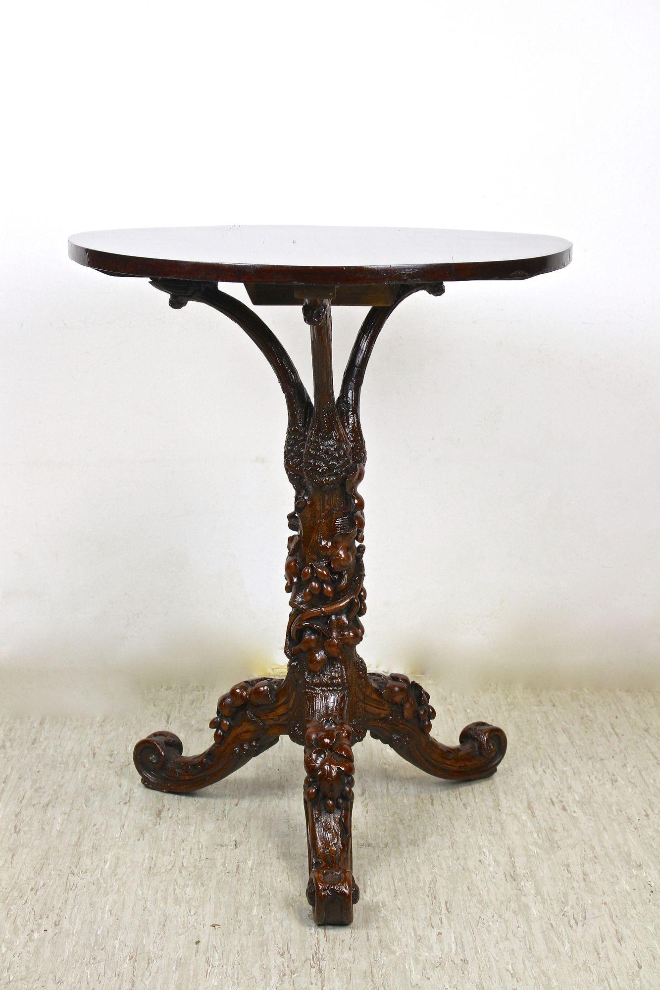 Exceptional 19th century rustic black forest side table, elaborately hand carved around 1880 in Austria. A one of a kind crafted Black Forest table with fantastic vine-theme carvings. Standing on three extraordinary designed feet, the base looks a