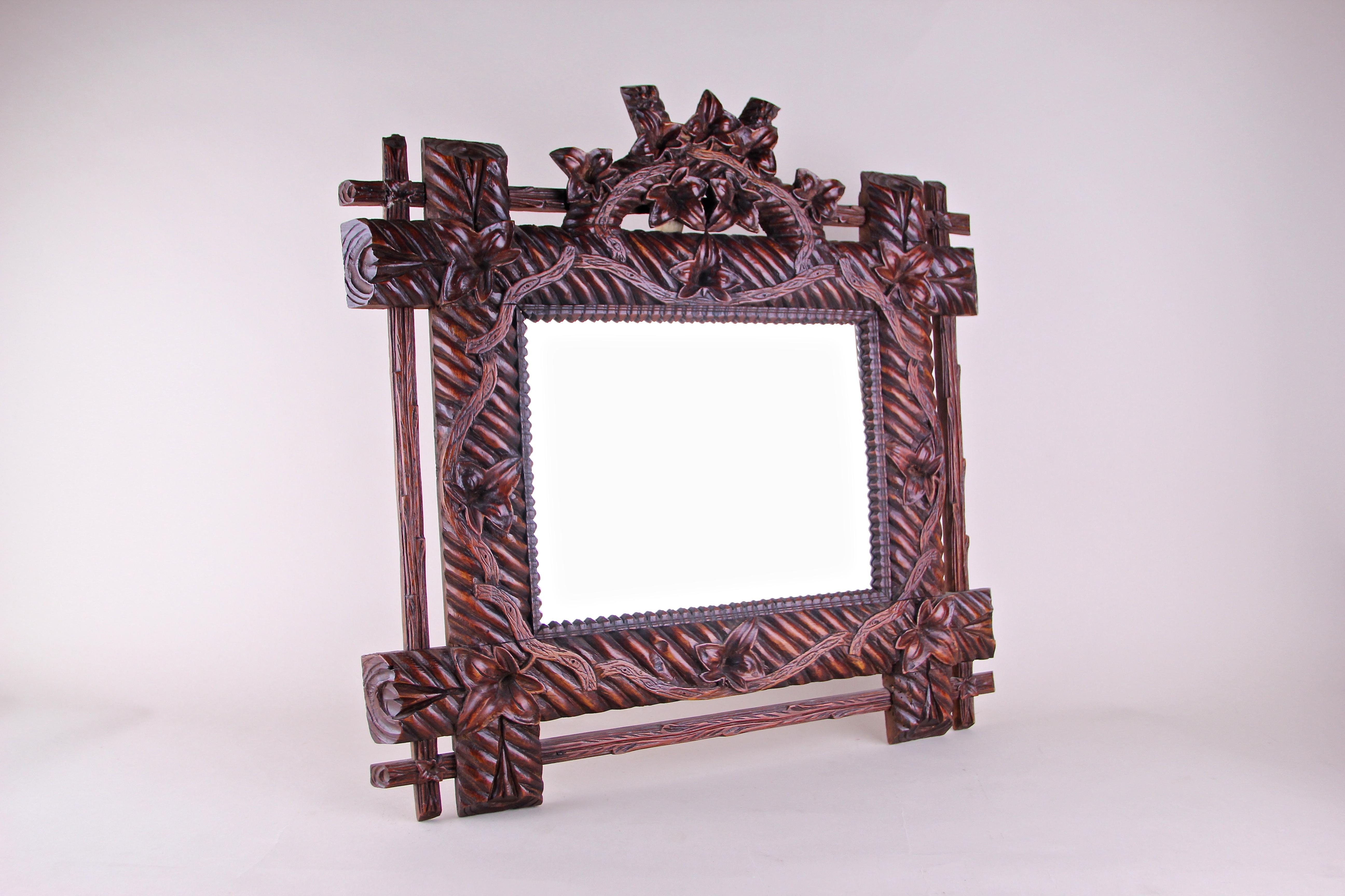 Exceptional Black Forest wall mirror out of Bavaria/ Germany from the late 19th century around 1880. An unusual designed rustic wall mirror with a wide dark brown glazed frame showing delicate hand-carved bellflowers and tendrils surrounded by four