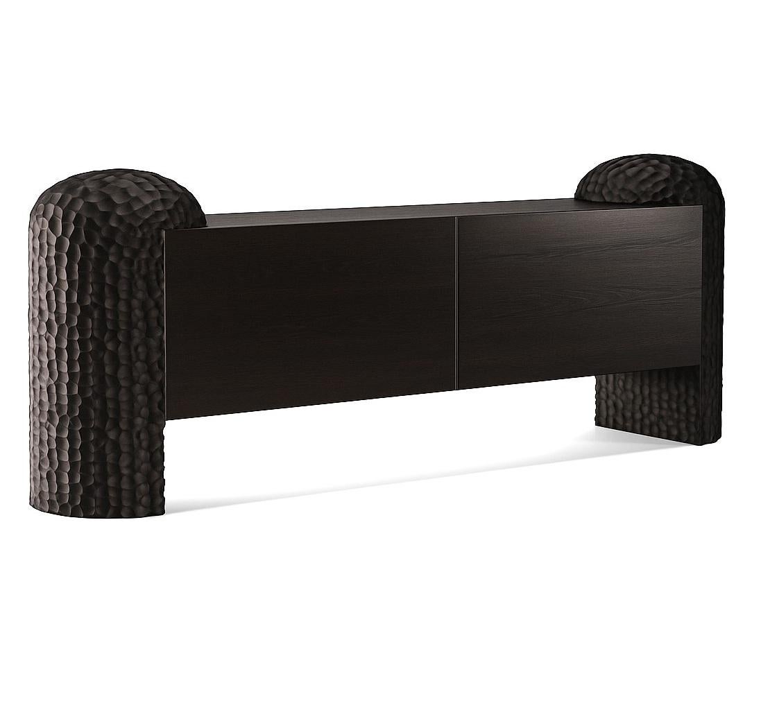 A sculptural statement piece rooted in nature, the Black Forest Sideboard is defined by its bold, hand-carved legs—monumental forms that evoke ancient tree trunks or forest columns. Between them, a minimalist body in wood veneer appears to float,