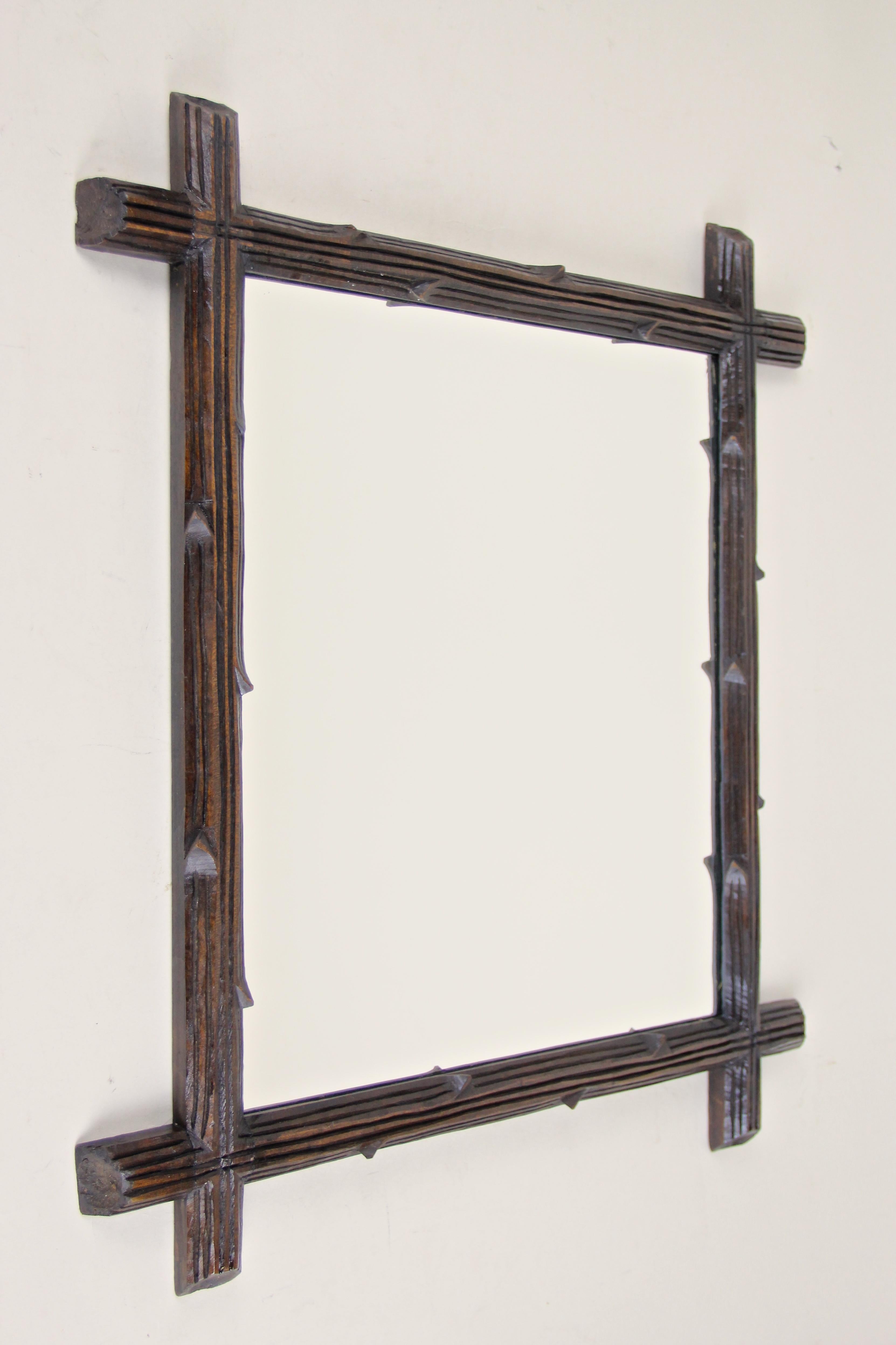 Mid-sized rustic Black Forest wall mirror from Austria, circa 1880. Beautifully hand carved out of basswood this late 19th century wall mirror shows a tree branch styled frame combined with a dark brown/ black surface which was sealed by a mat